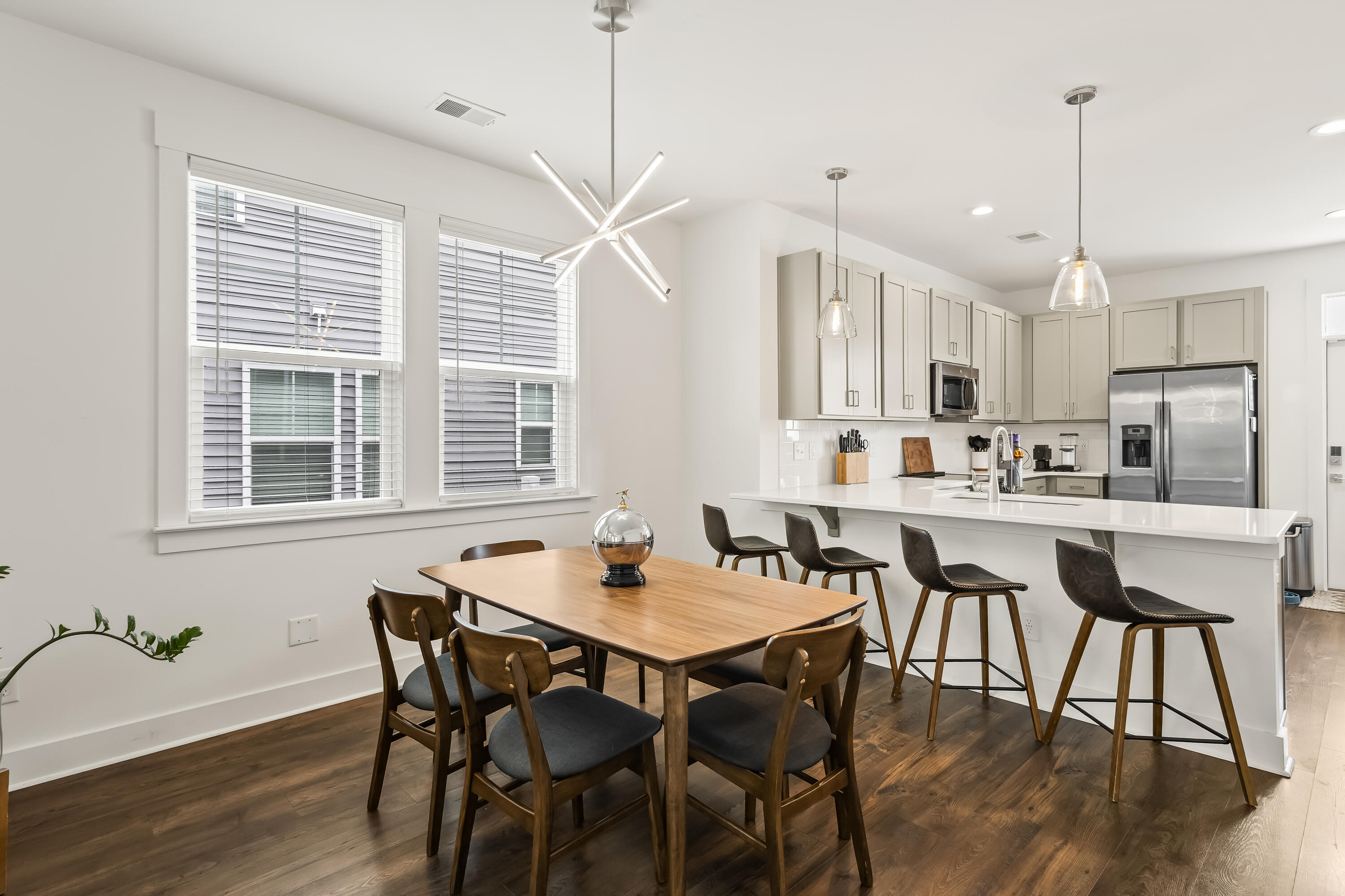 Dining area with a wood table beside a white kitchen island and stainless steel appliances.