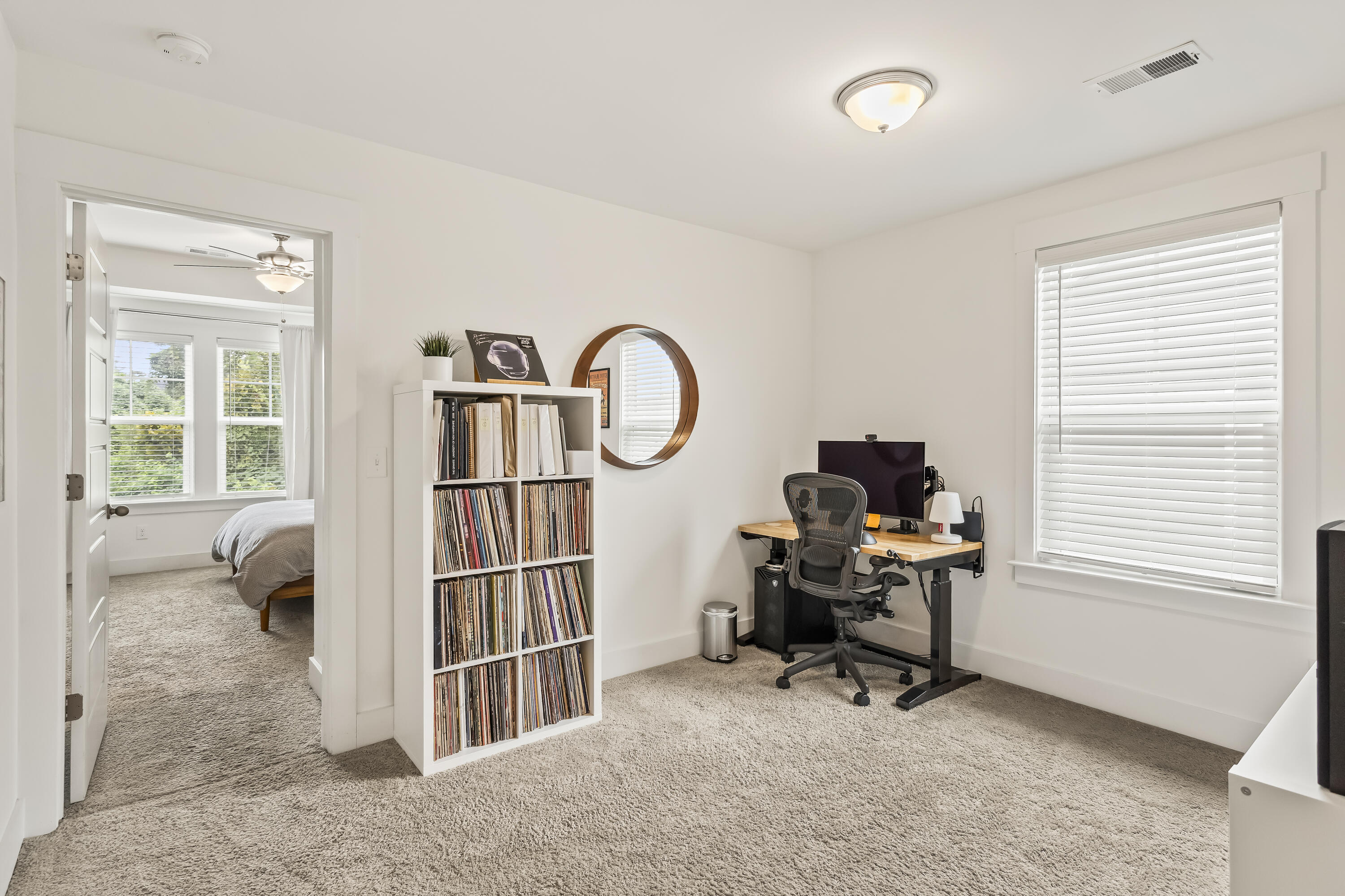 Home office with a record-filled bookcase, desk, and doorway to a bedroom