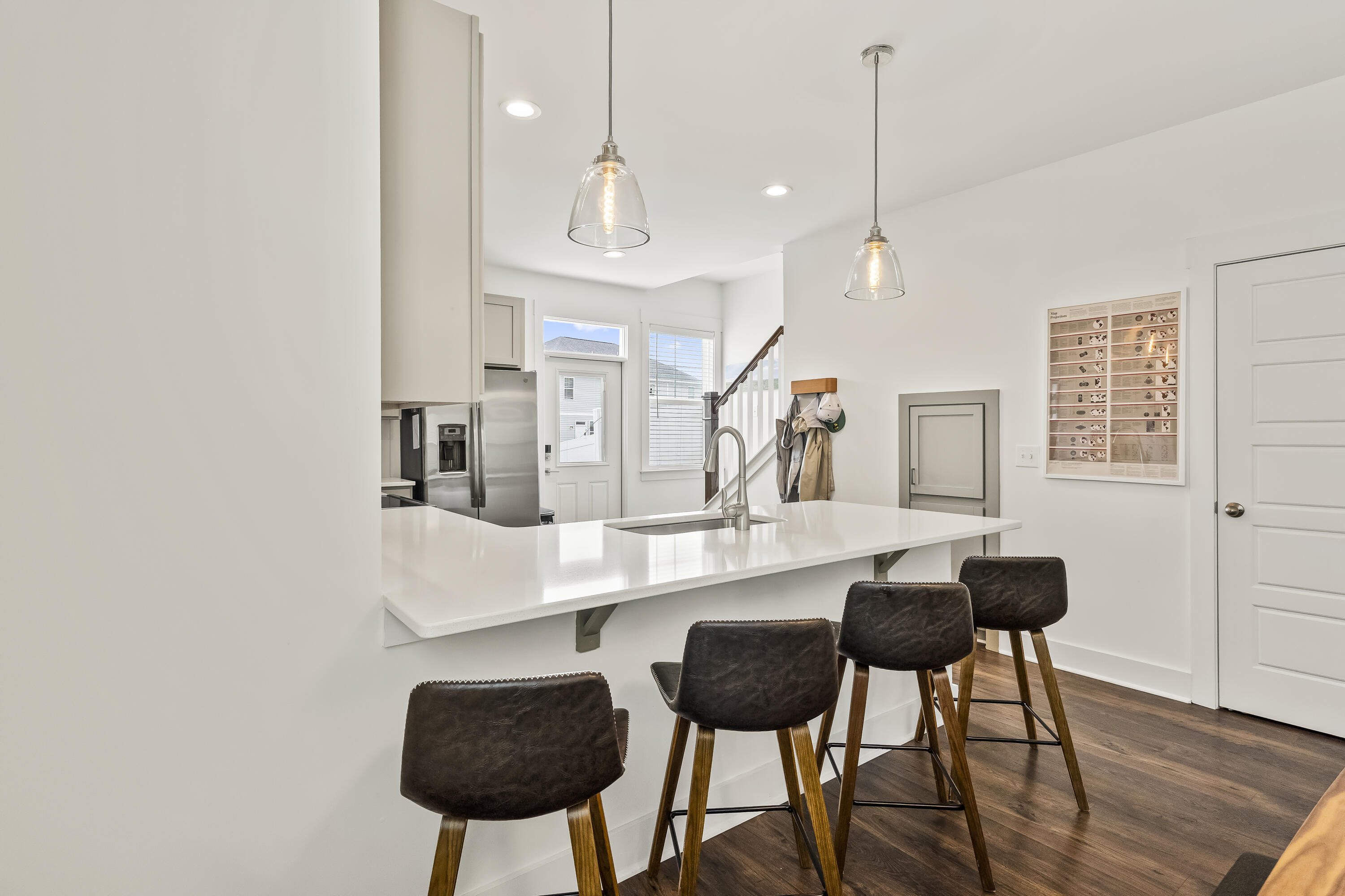 Bright kitchen with a white island, dark bar stools, stainless appliances, and pendant lights.