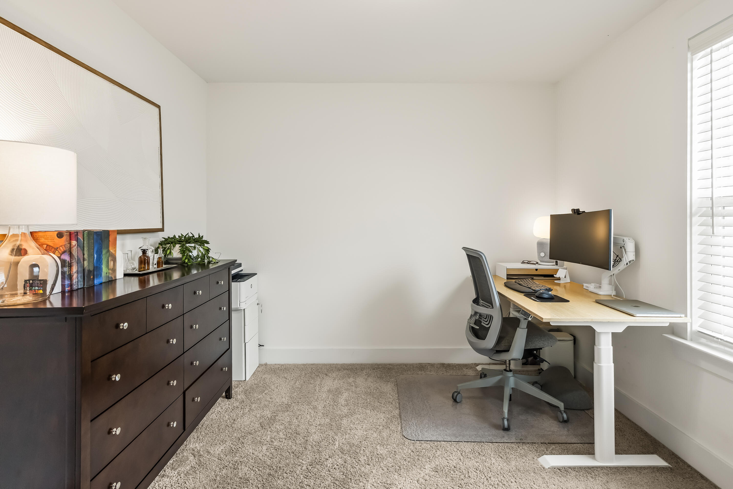 Furnished home office with a standing desk, ergonomic chair, and dark dresser.