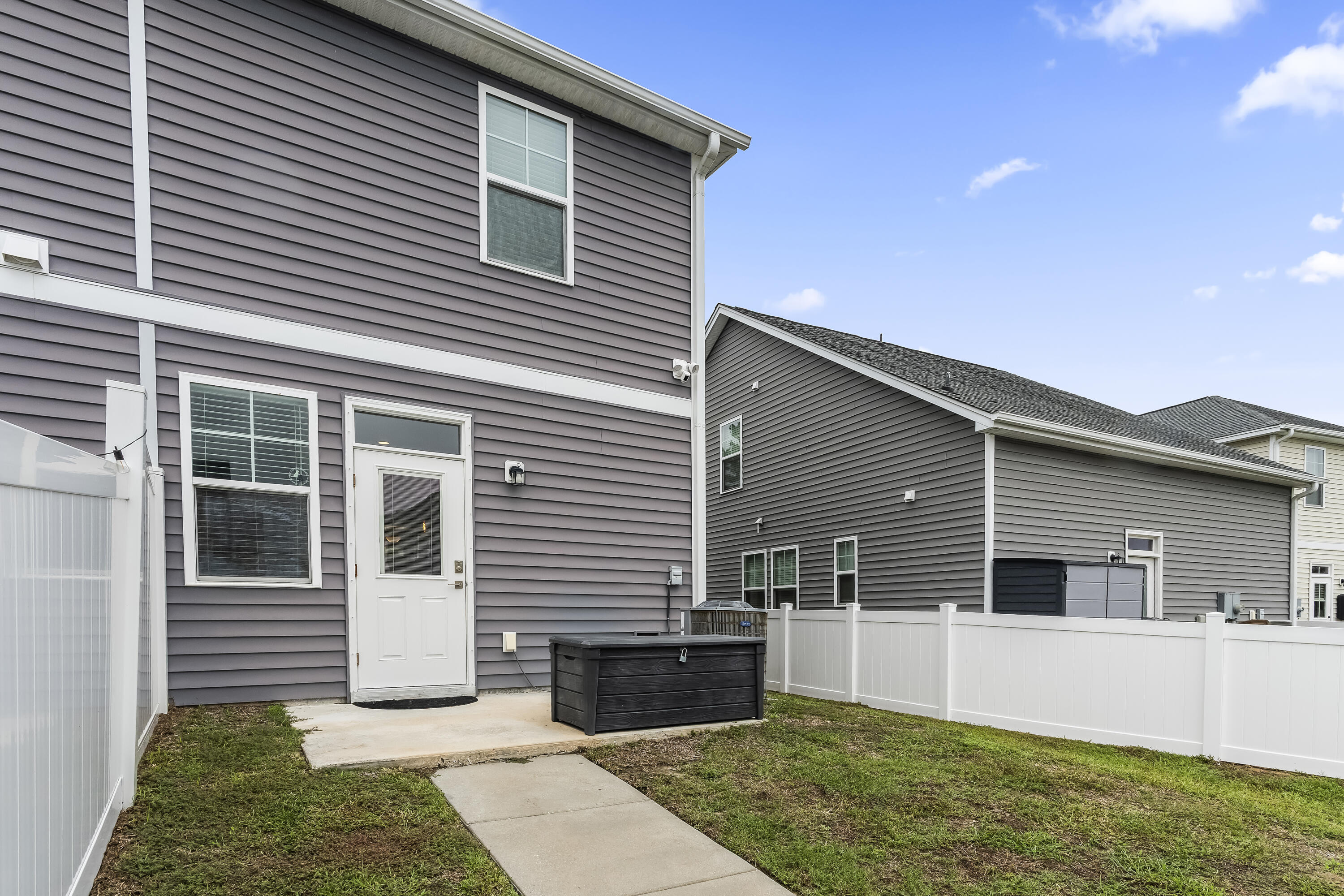 Gray two-story home's backyard with a white privacy fence, concrete patio, and black hot tub.