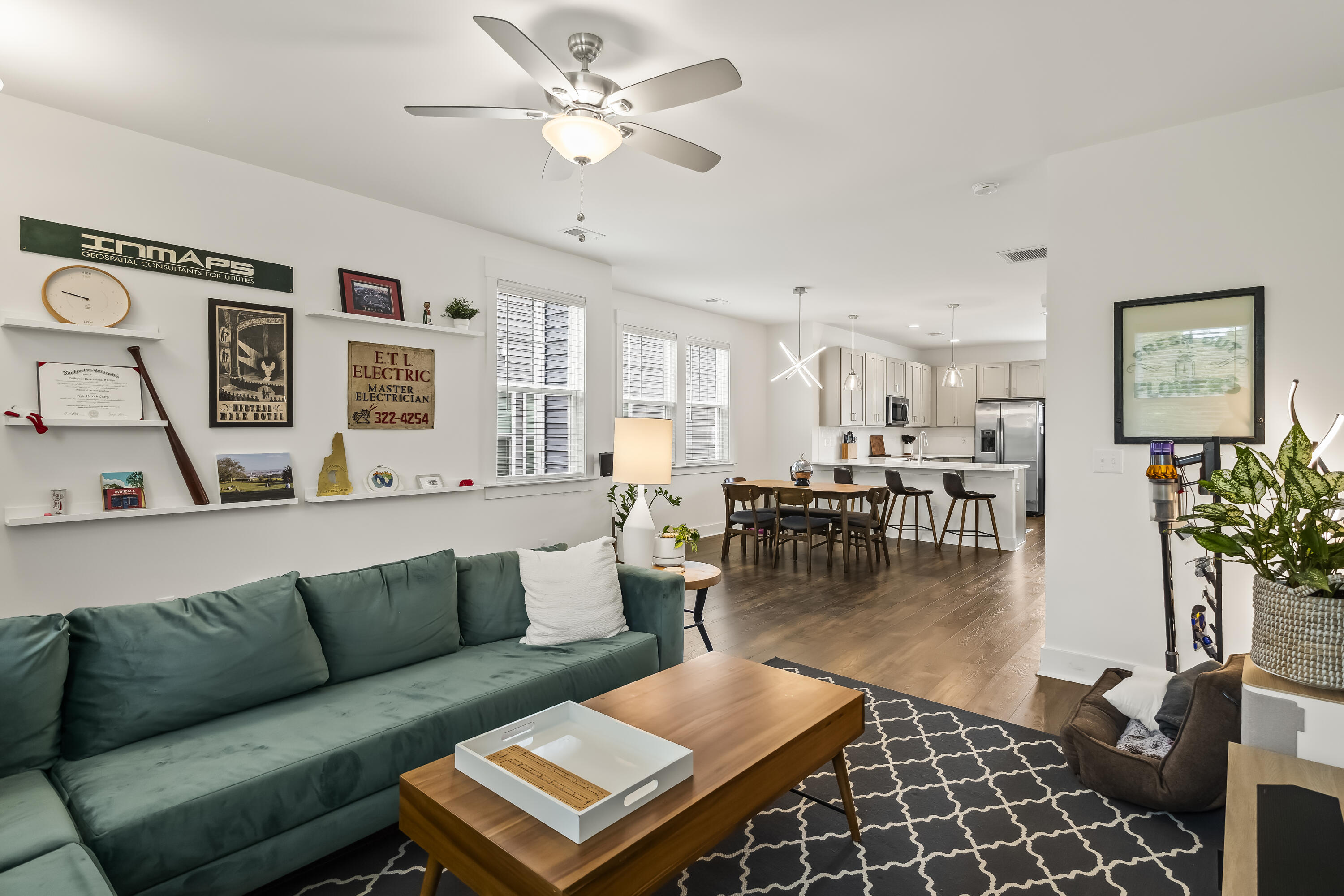 Open-plan living room with teal sectional, patterned rug, dining table, and white kitchen beyond.