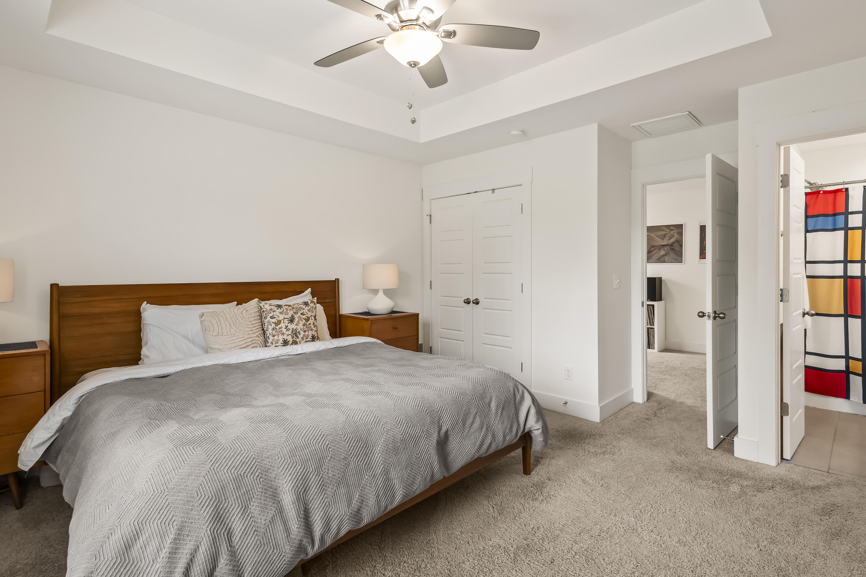 Bedroom with a wooden bed, gray patterned bedding, ceiling fan, and white double closet doors.