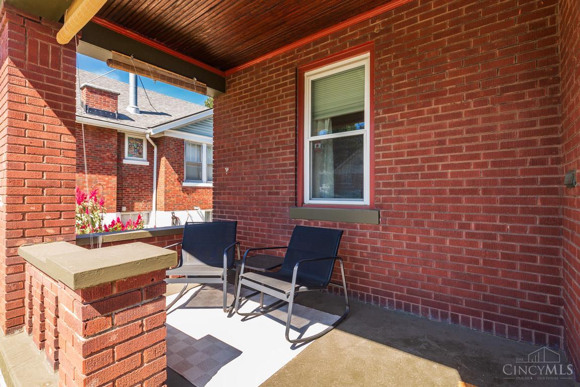Covered brick patio with two dark chairs beneath a wood-plank ceiling.