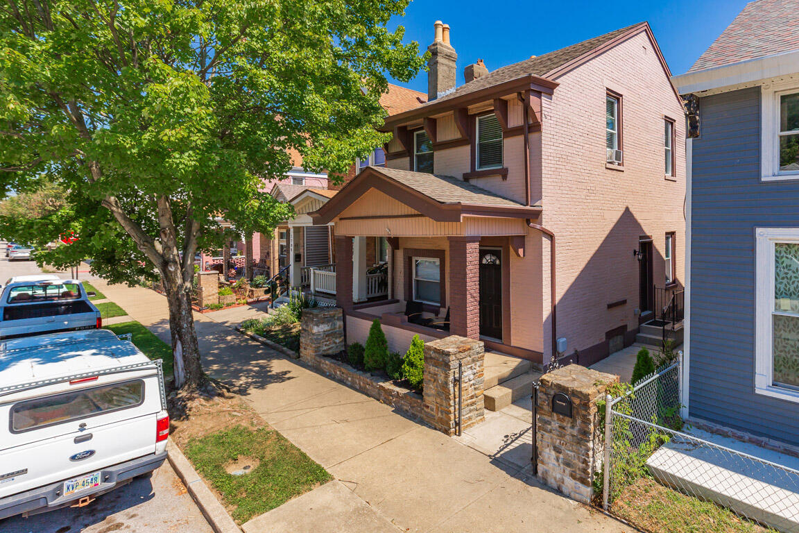 Two-story pink brick house with a covered porch and stone gate pillars beneath a large shade tree.