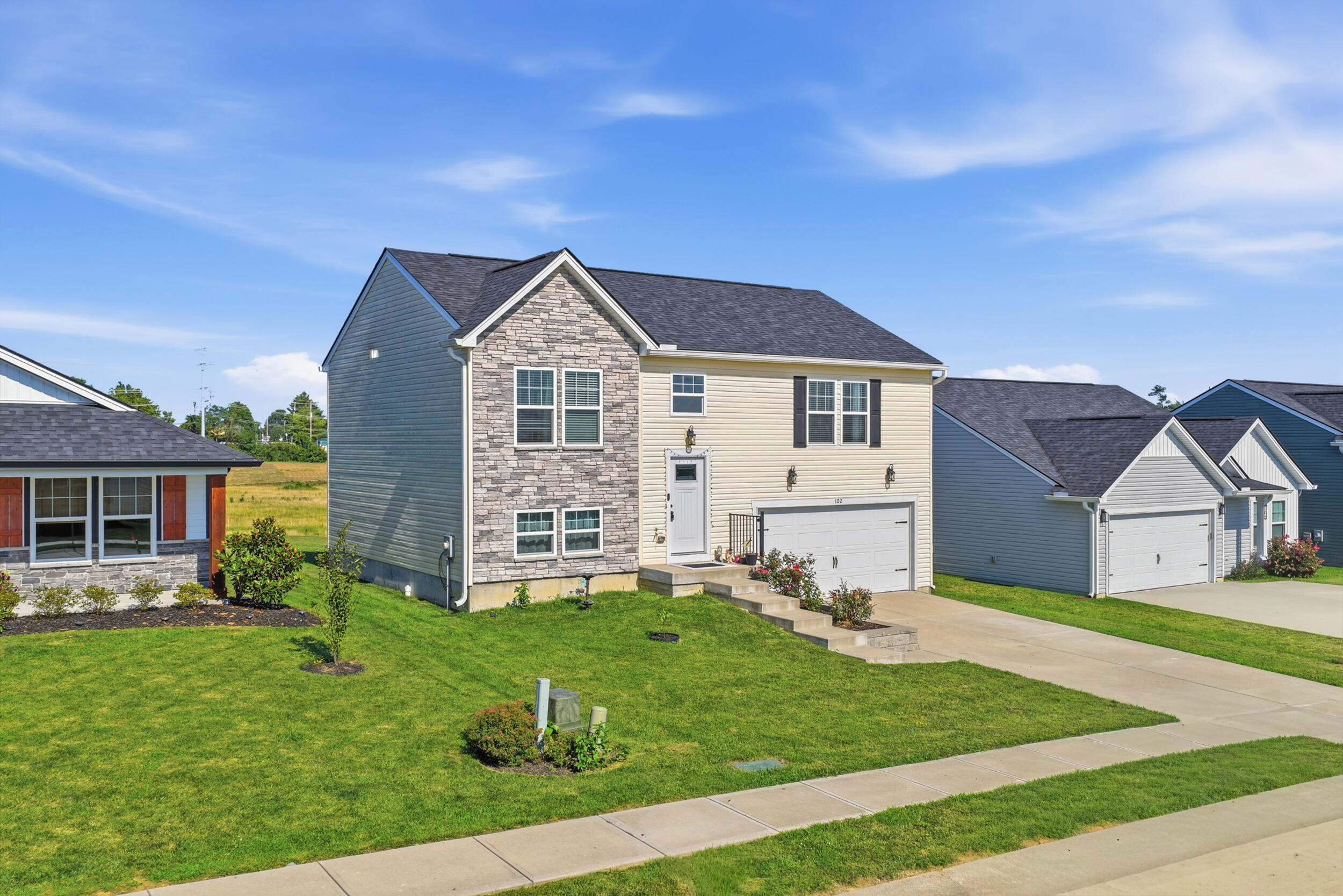 Two-story stone-and-siding house with an attached garage, green lawn, and neighboring homes.