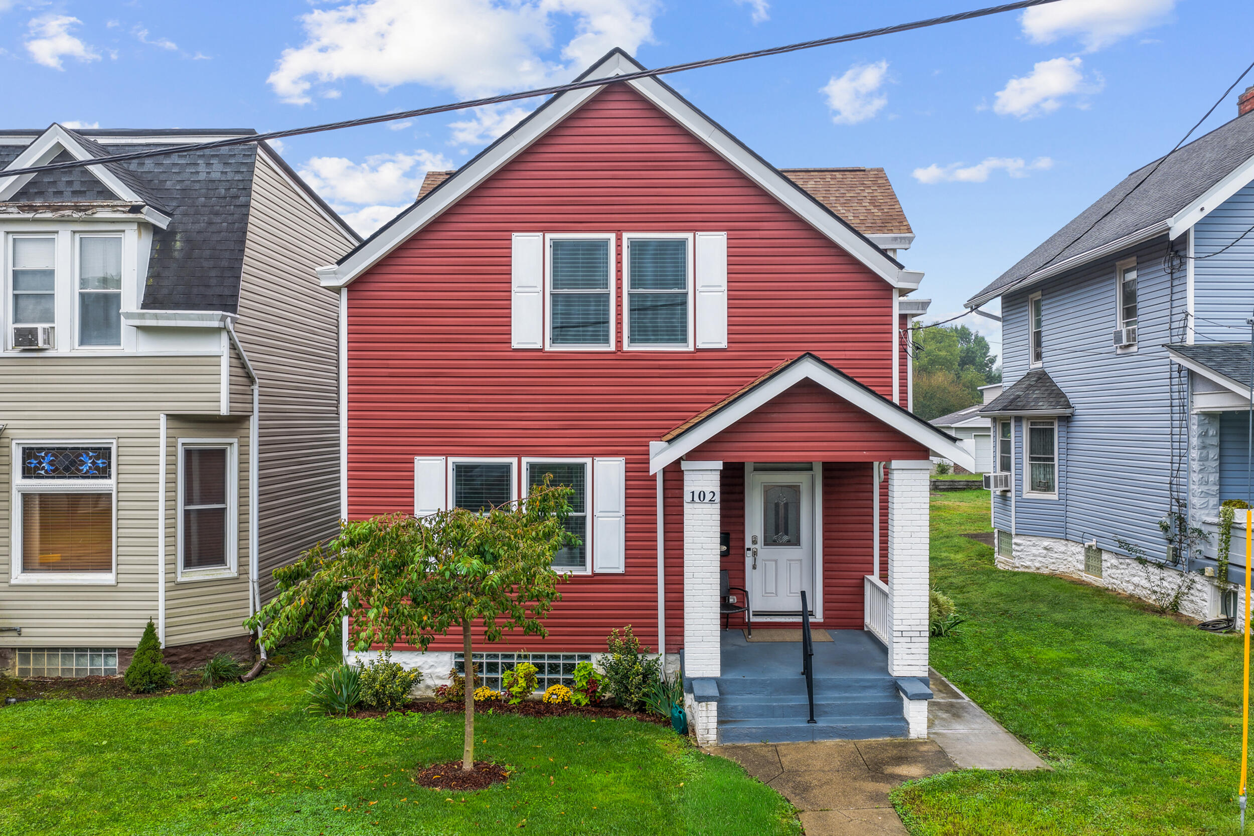 Red two-story house with white shutters, a covered porch, and landscaped front lawn.
