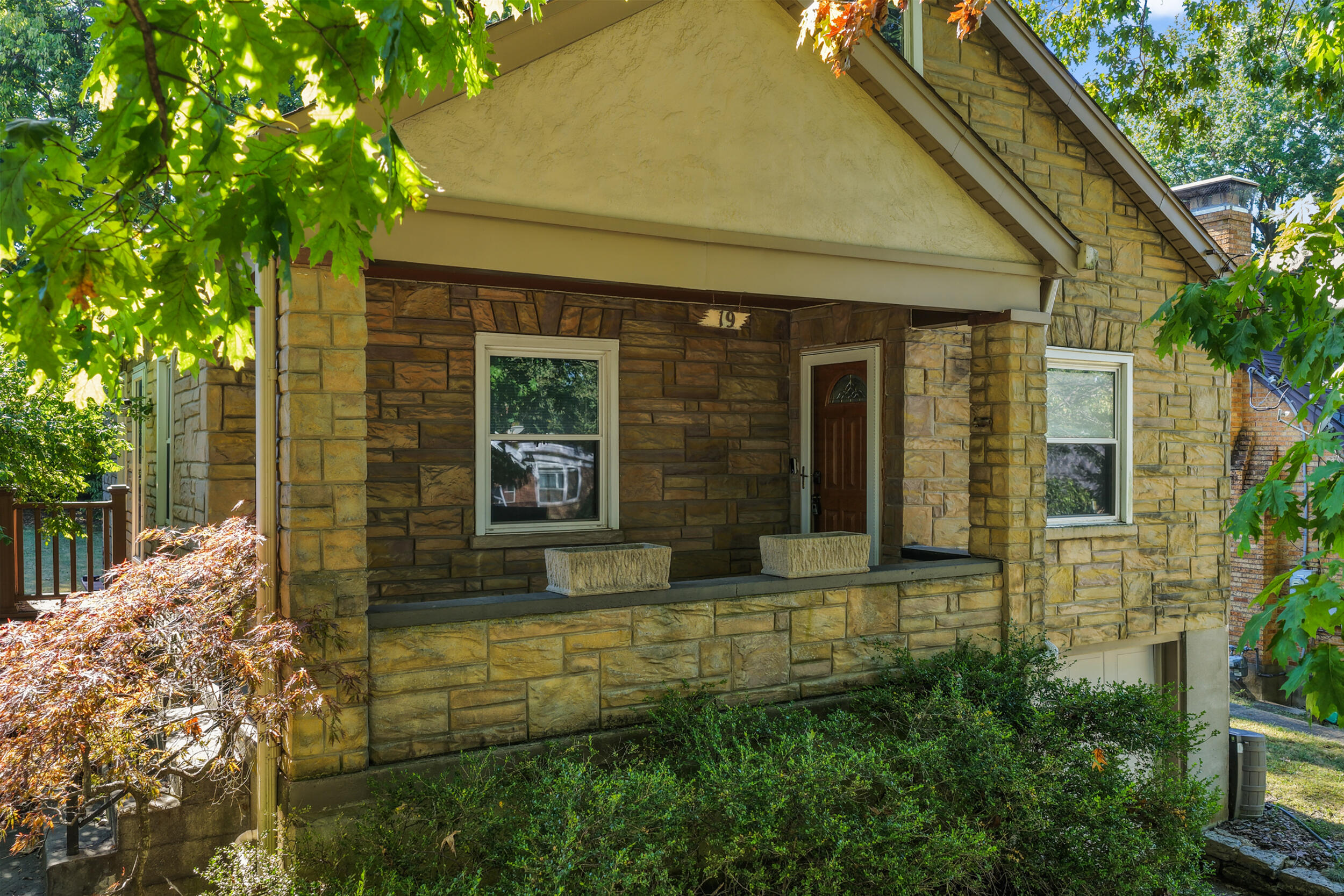 Stone house with a covered porch and leafy trees surrounding it.