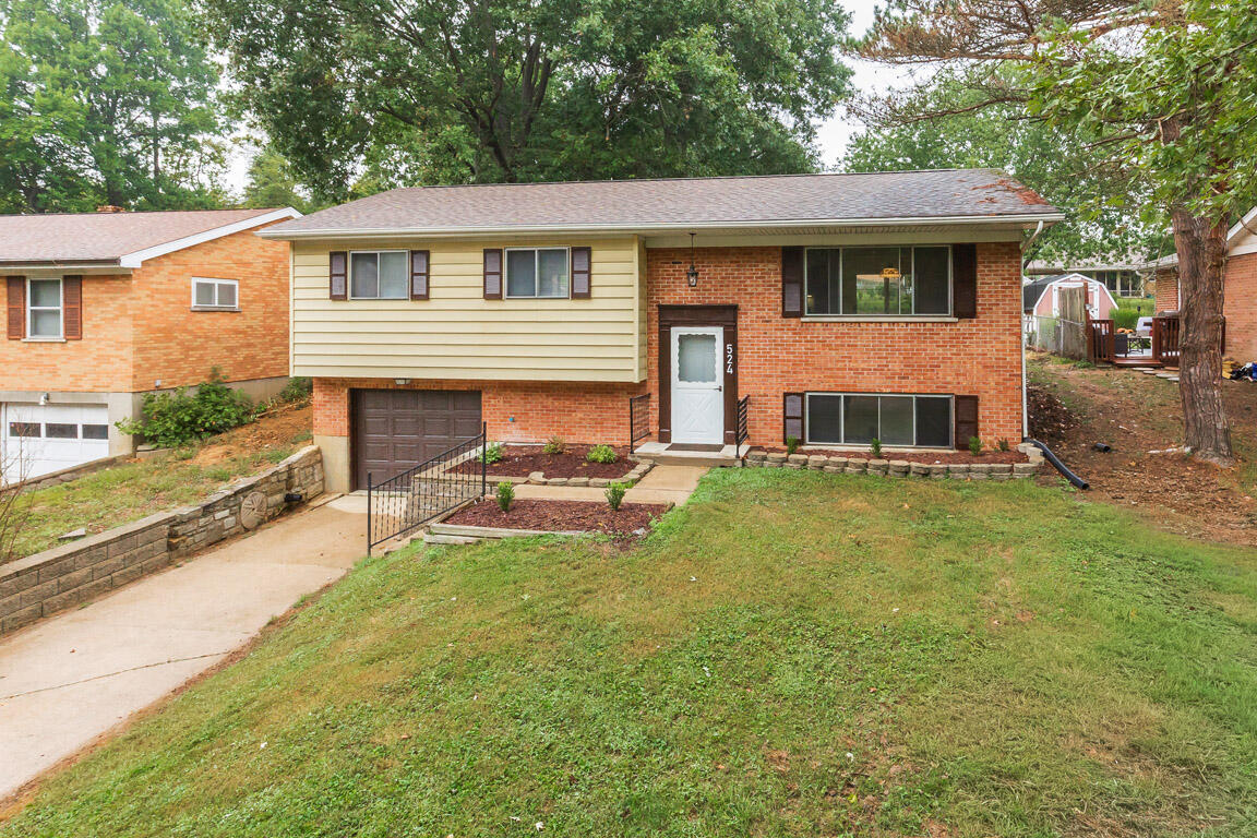 Split-level brick and yellow-sided home with an attached garage and sloping front lawn.