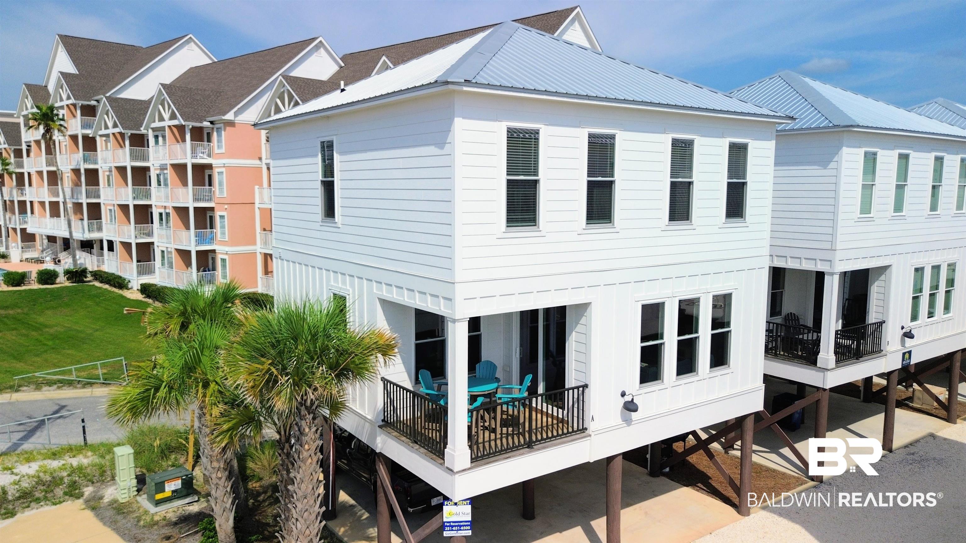 Raised white coastal home with a silver metal roof, dark-railed balconies, and palm trees.