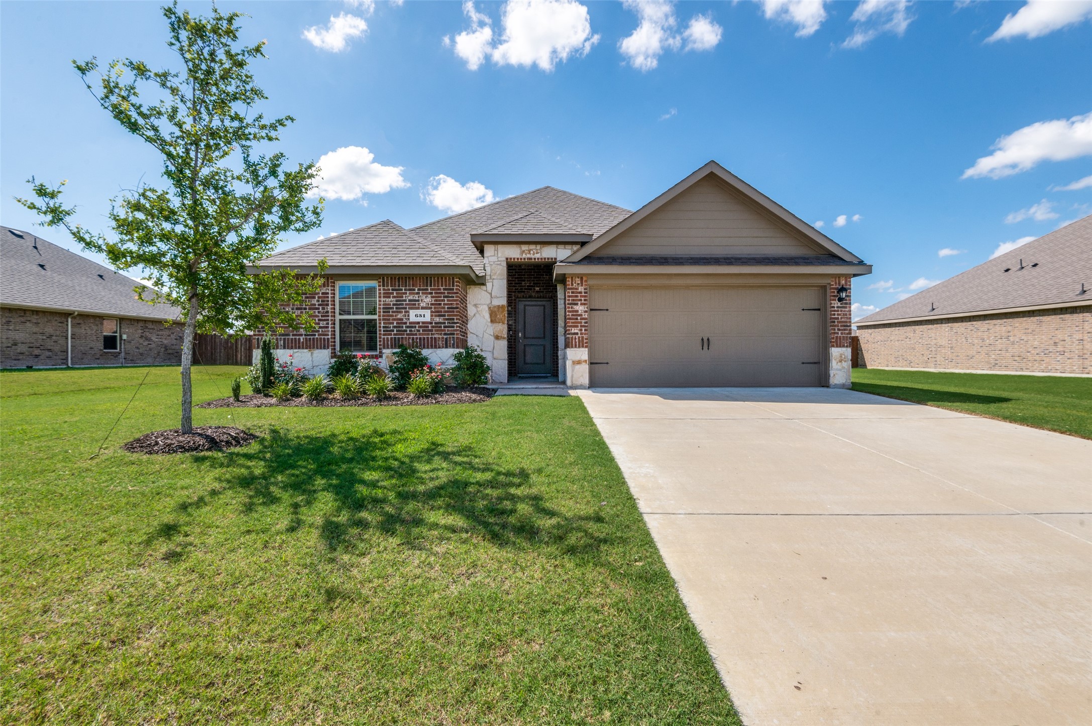 Brick home with stone accents, a two-car garage, landscaped lawn, and wide driveway.