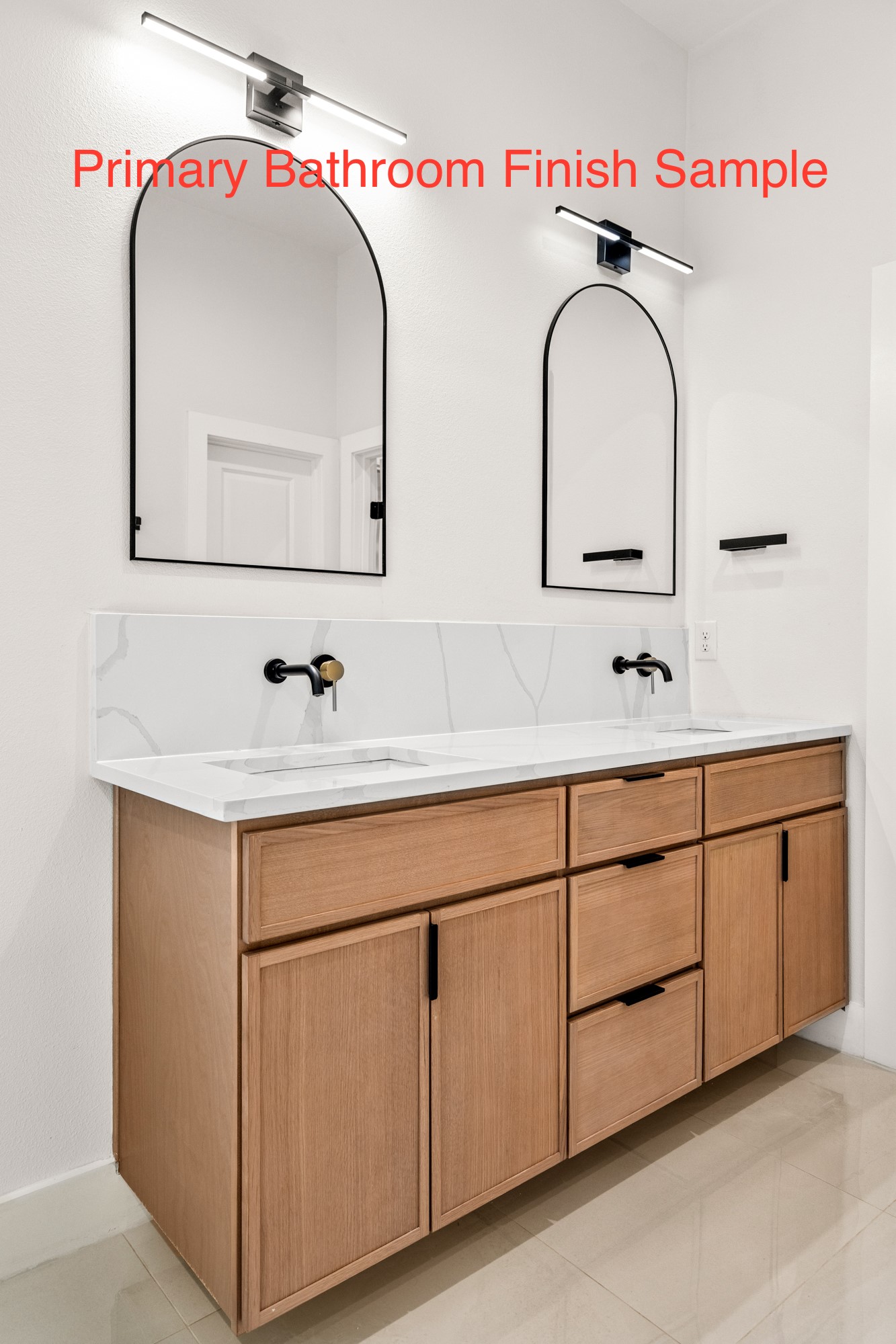 Primary bathroom vanity with light wood cabinetry, a white veined counter, black faucets, and arched mirrors.