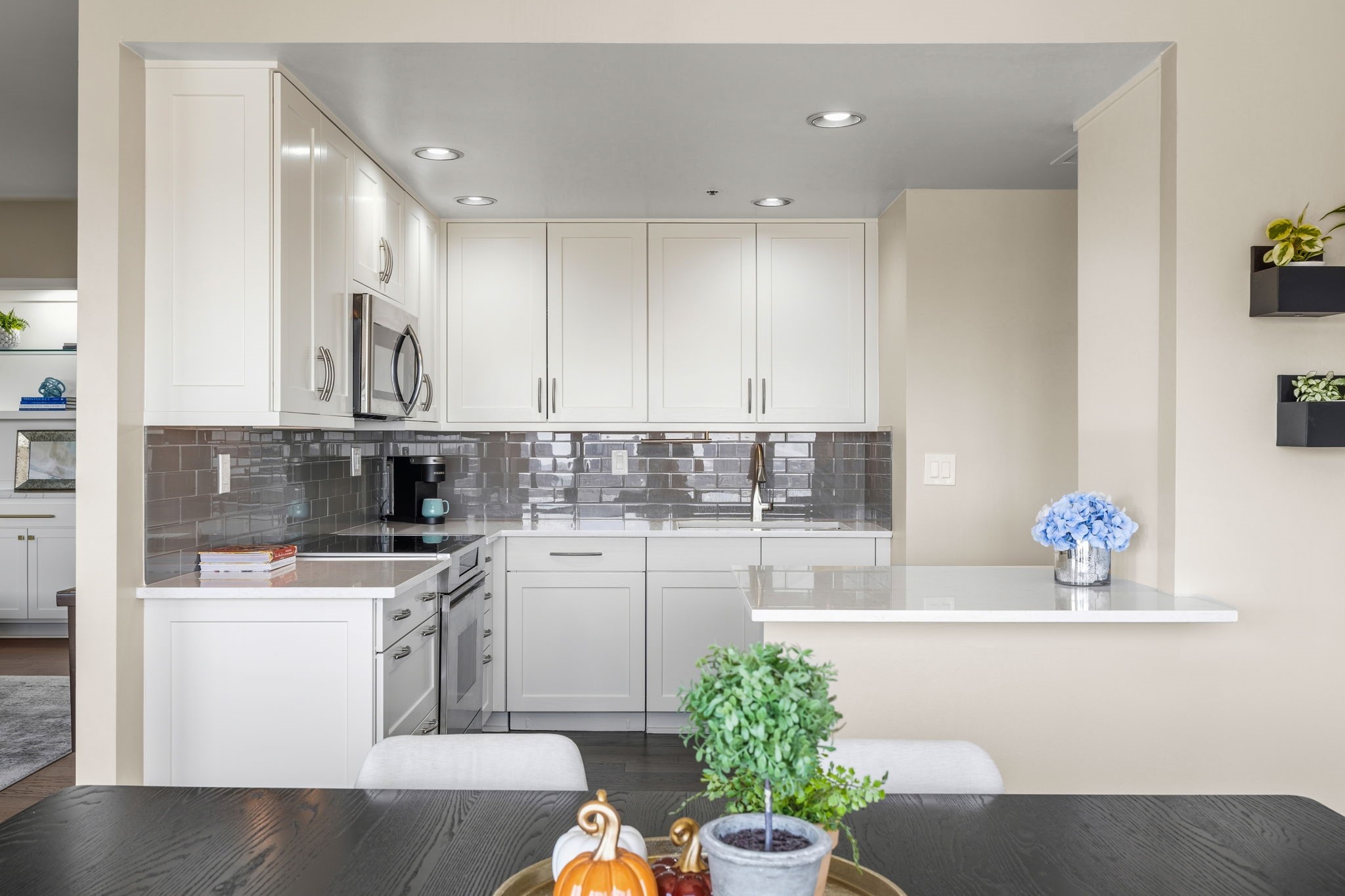 Kitchen with white cabinets, stainless appliances, gray tile backsplash, and a white peninsula.