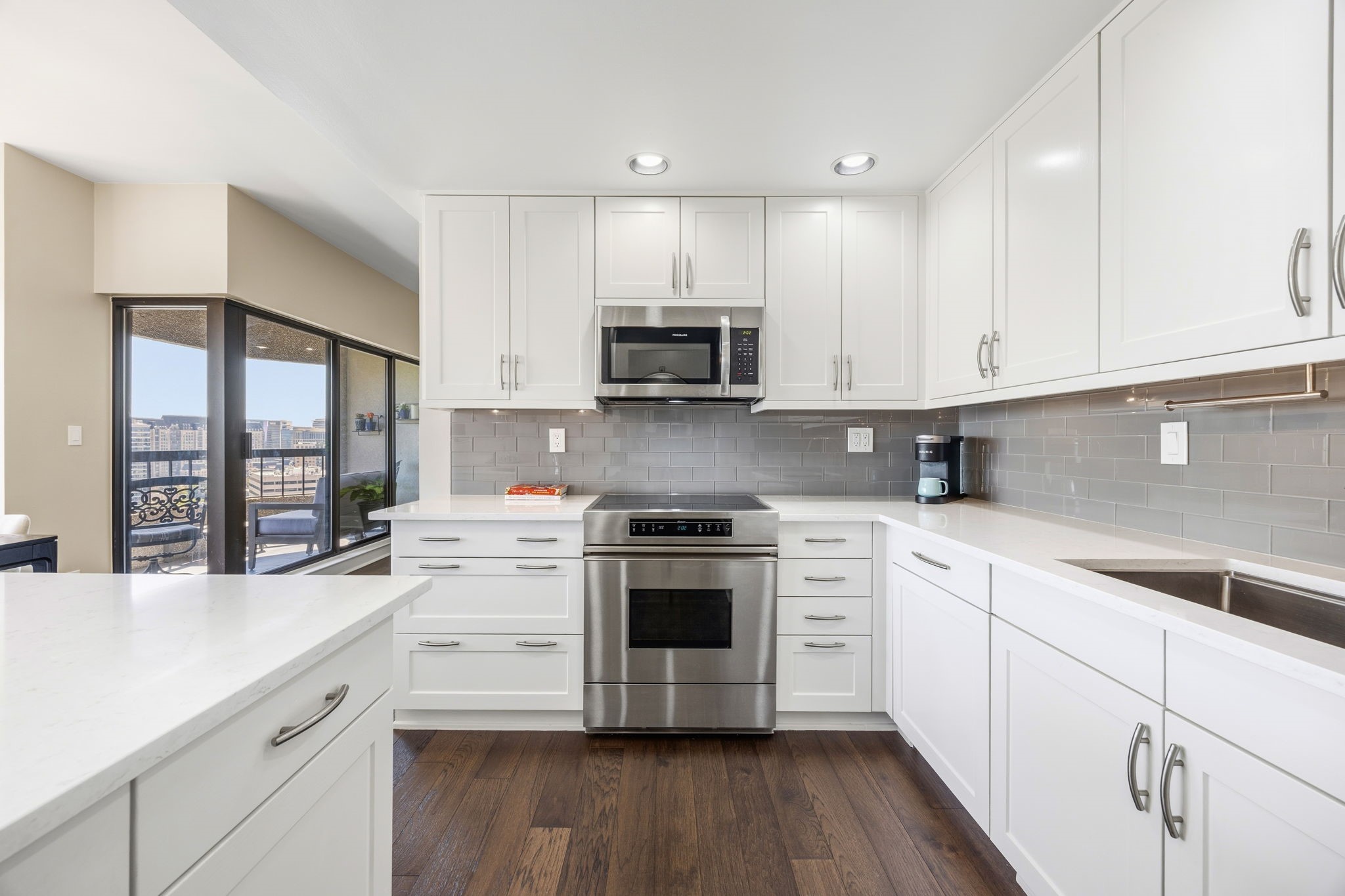 Condo kitchen with white cabinets and stainless appliances, opening onto a balcony with city views.