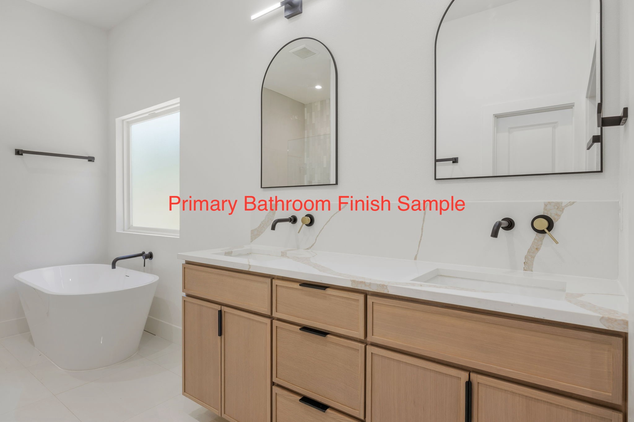 Primary bathroom with freestanding tub, light wood double vanity, stone countertop, and arched mirrors.