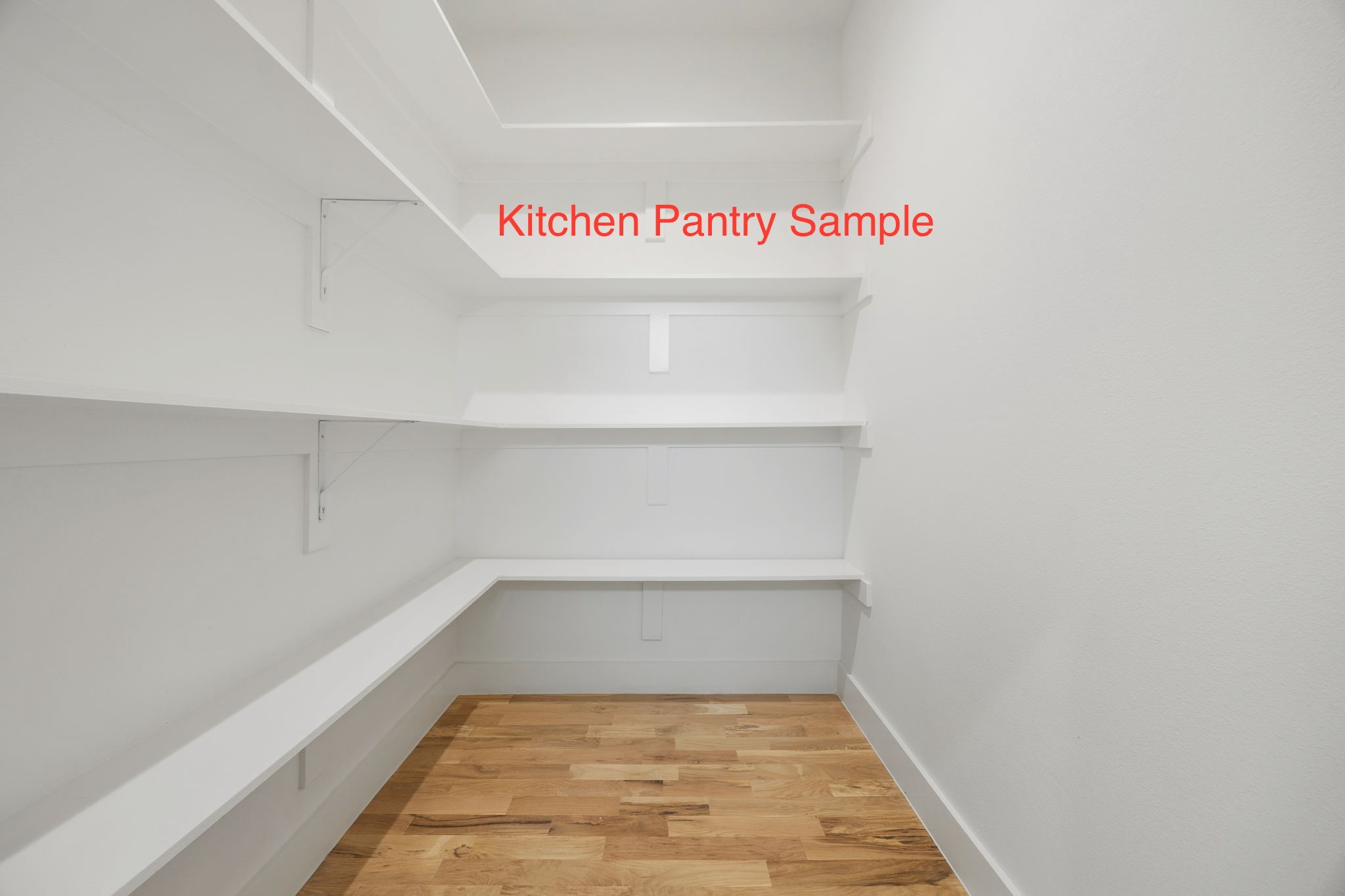 Empty walk-in pantry with white wraparound shelves and a wood plank floor.
