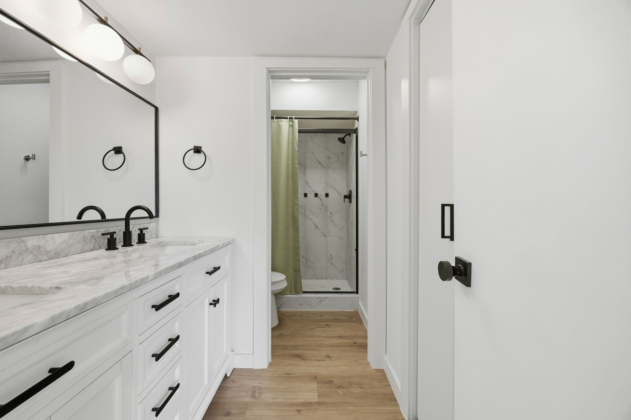 Bathroom with a veined marble vanity, black fixtures, and a walk-in shower with a green curtain.
