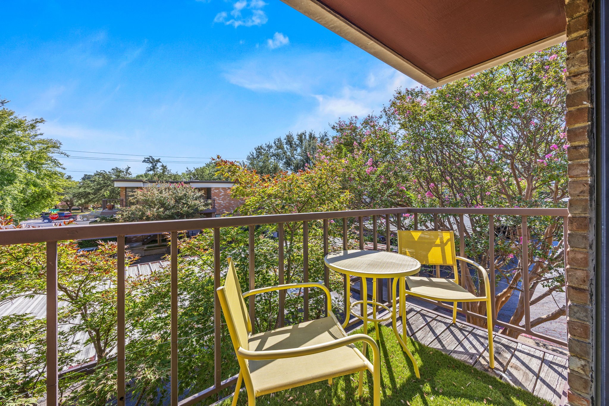 Apartment balcony with yellow chairs and table overlooking flowering trees.