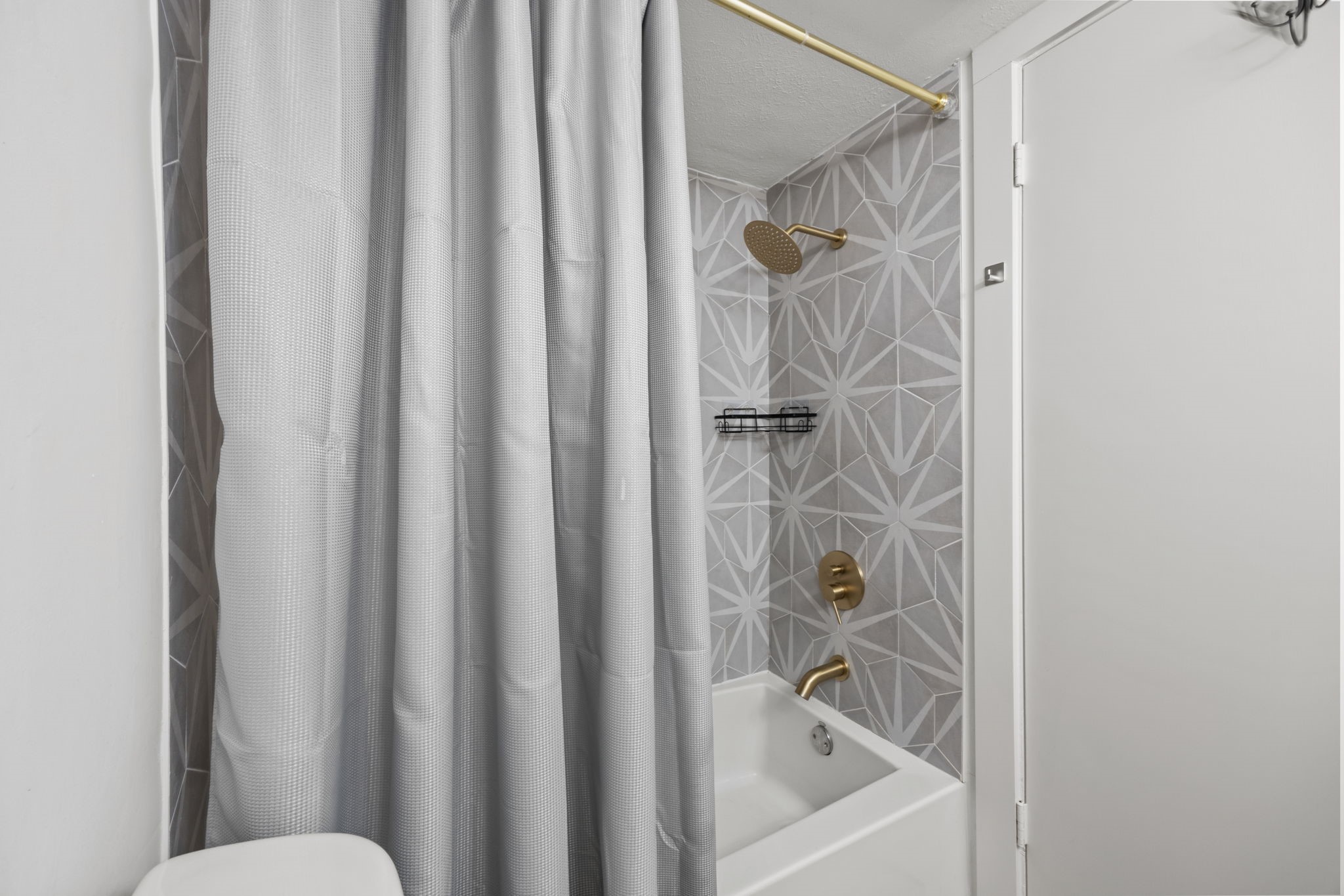 Bathroom tub and shower with geometric gray tile and brass fixtures.