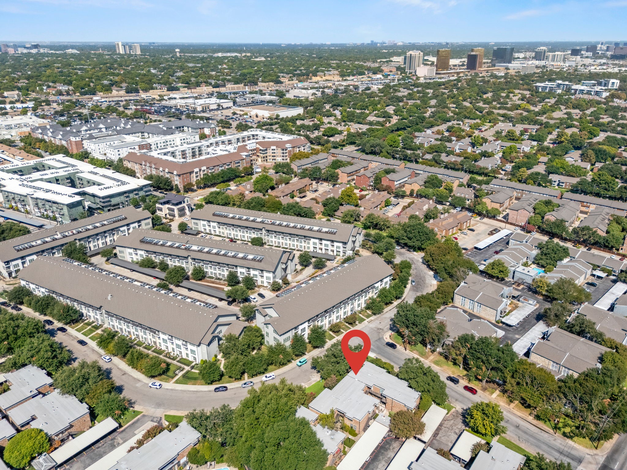Aerial view of a condominium community with a red location marker and distant city skyline.