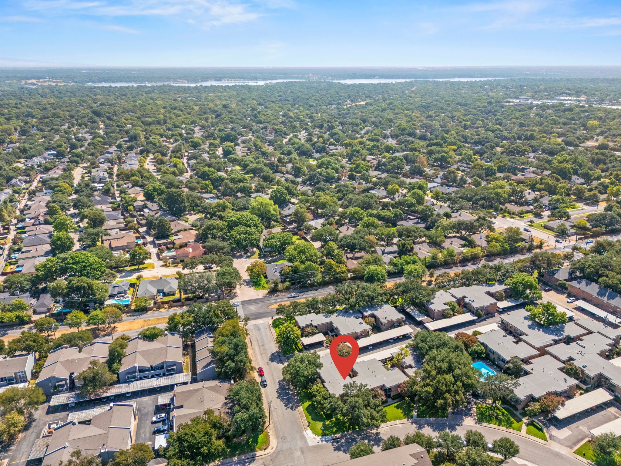 Aerial view of the marked condo complex among leafy homes, with a swimming pool and distant water.