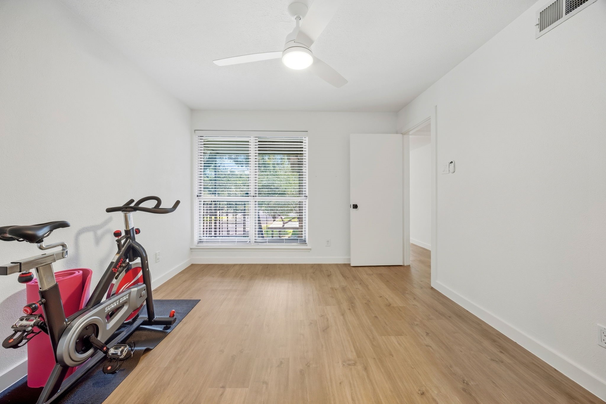Bright room with wood-look flooring, window blinds, and a stationary exercise bike.