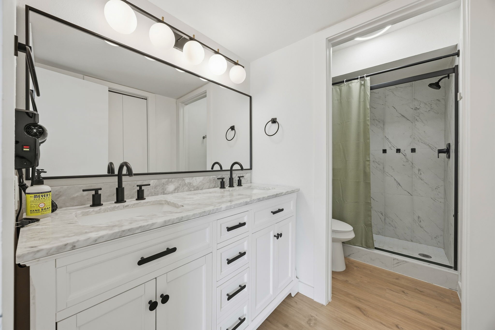 Bathroom with a marble double vanity, black fixtures, and a tiled walk-in shower.