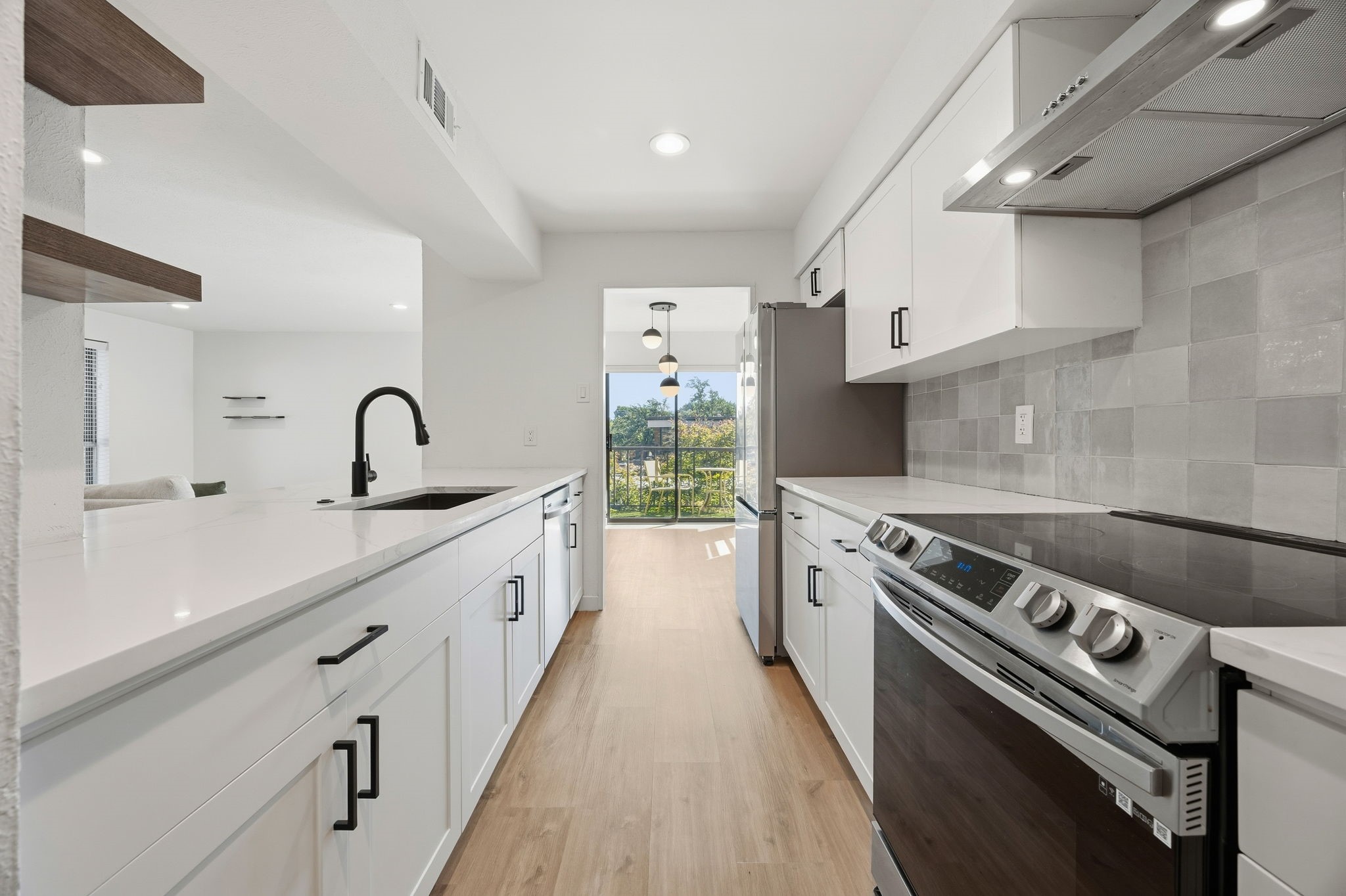 Modern white galley kitchen with a large island, stainless appliances, and a balcony view.