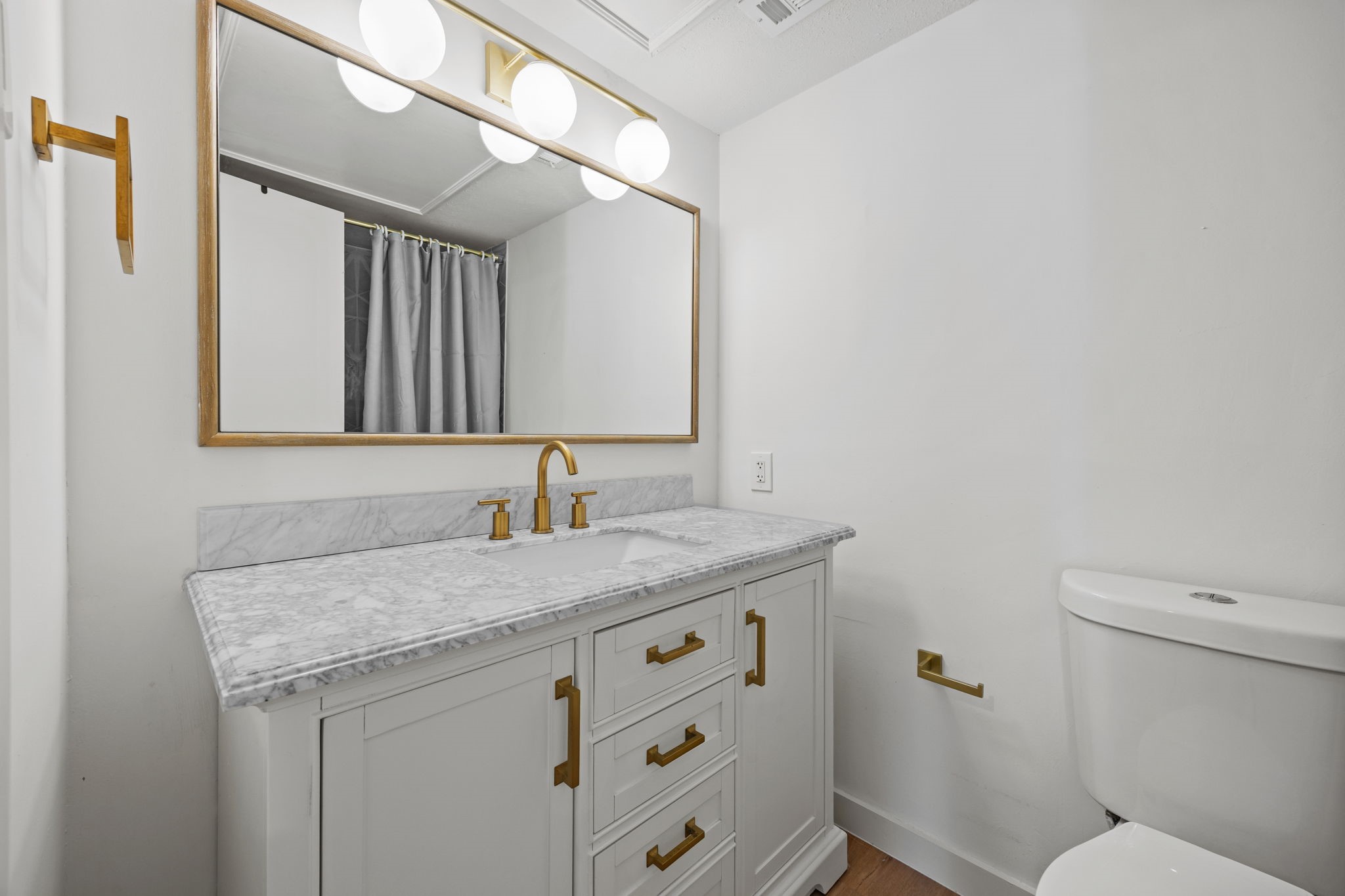 Bathroom vanity with marble counter, brass fixtures, wood-framed mirror, and adjacent toilet.