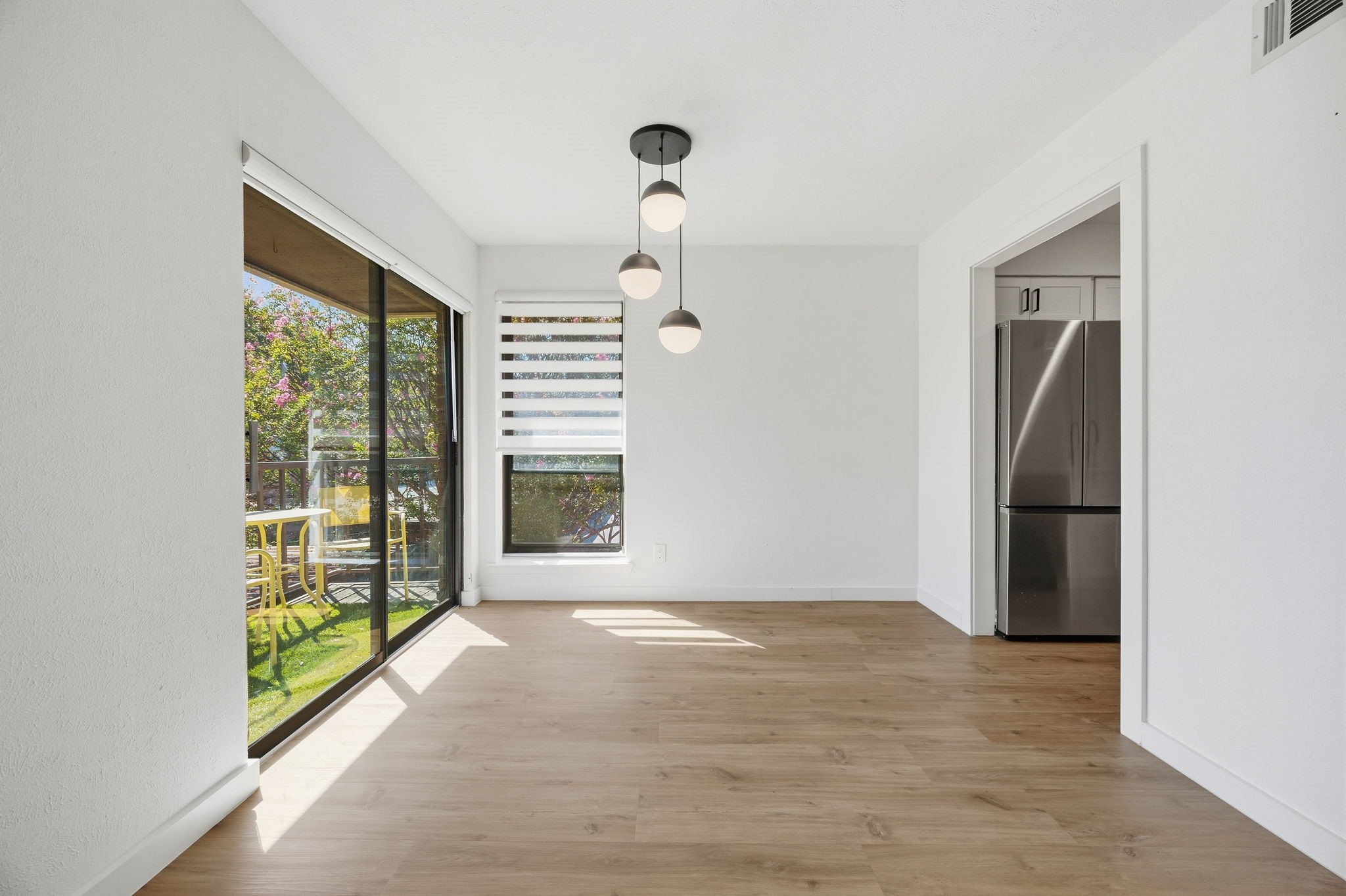 Vacant dining area with pendant lights, wood floors, and sliding glass doors to a leafy patio.
