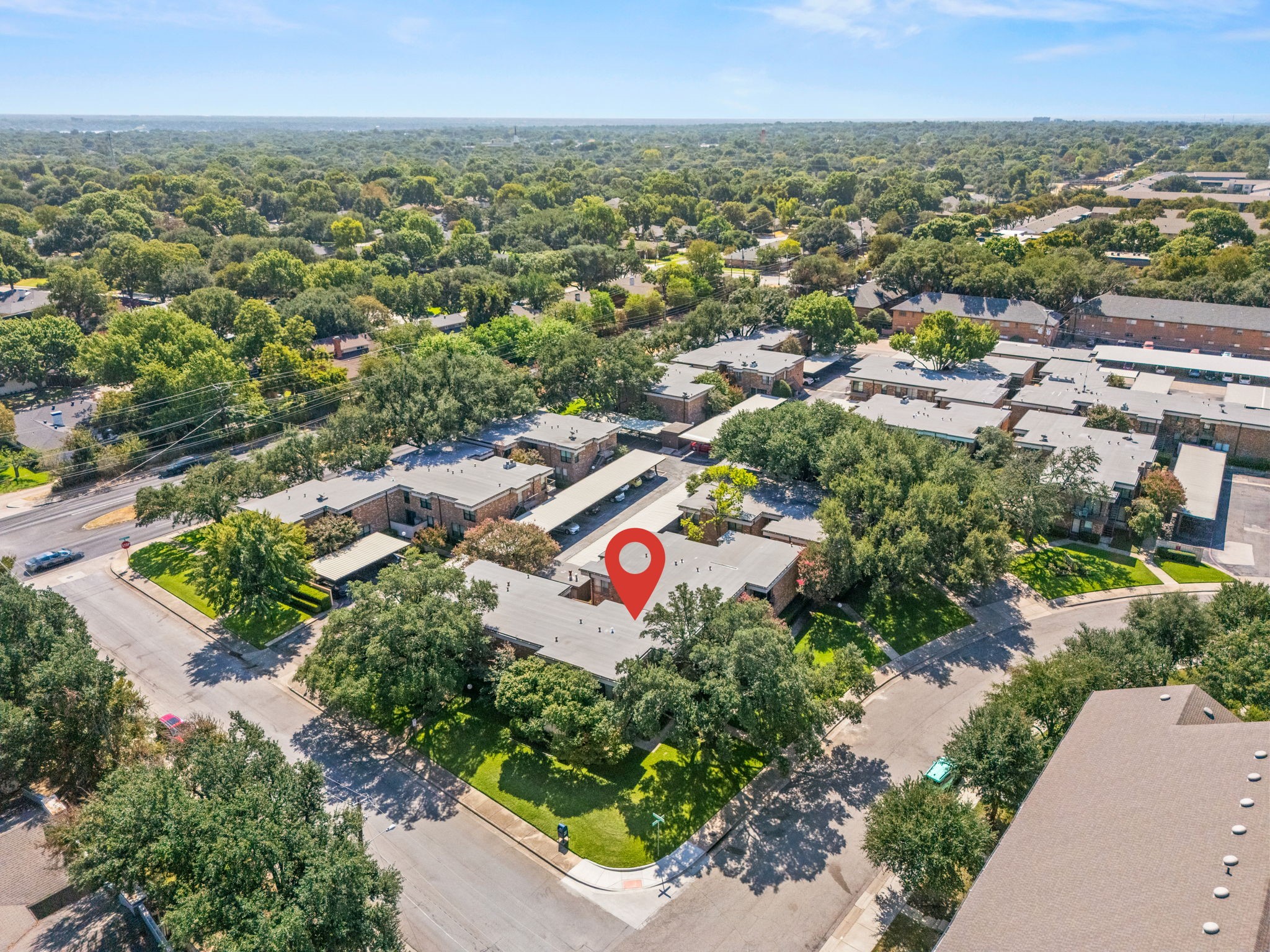 Aerial view of a brick residential complex among mature trees, with a red pin marking one building.