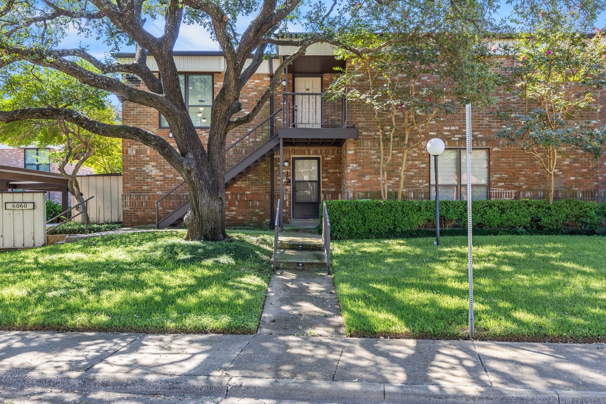 Two-story brick residence with exterior stairs, a broad shade tree, and a neatly trimmed front lawn.