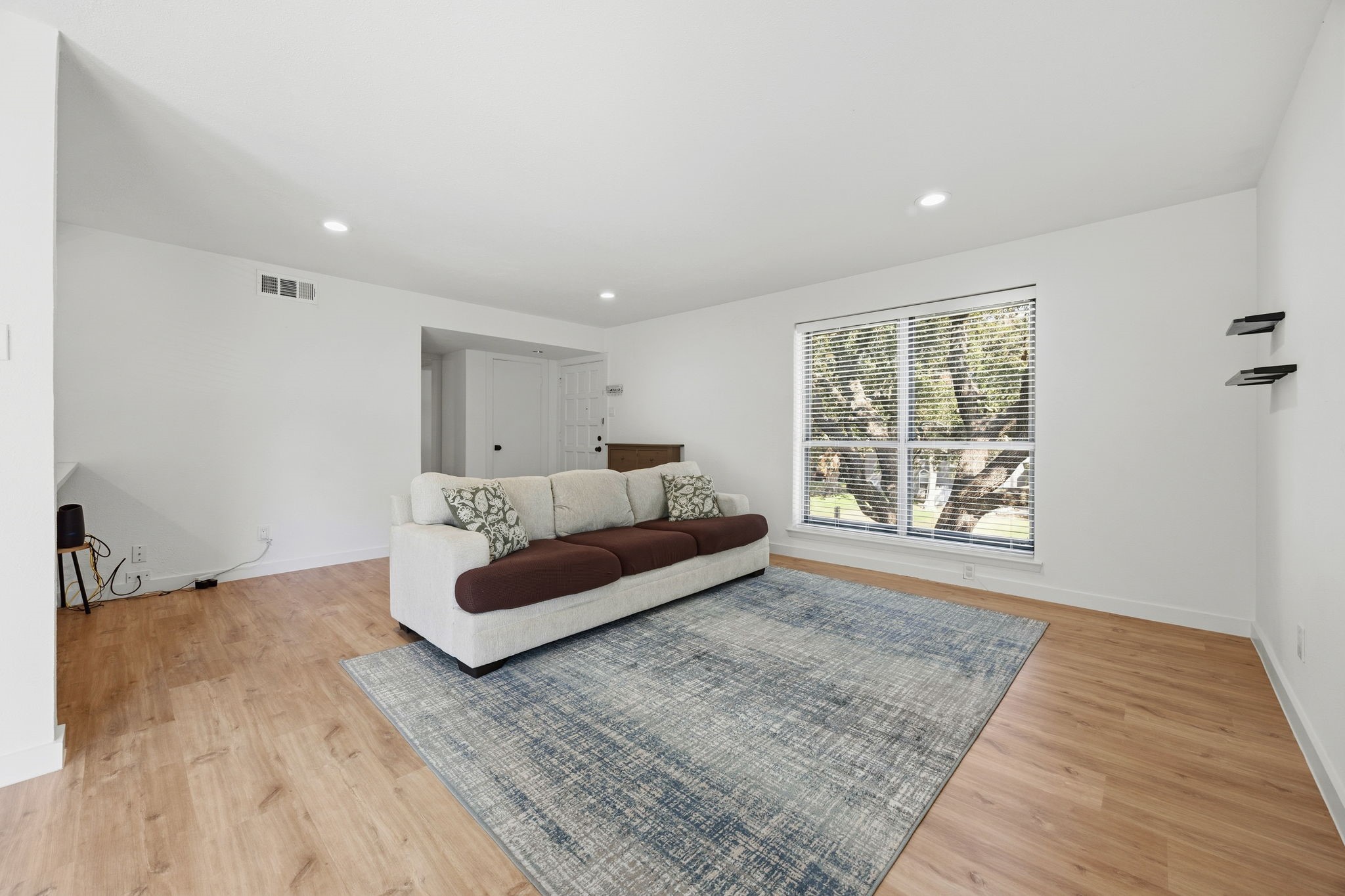 Living room with a cream sofa, patterned rug, light wood floors, and a large window.
