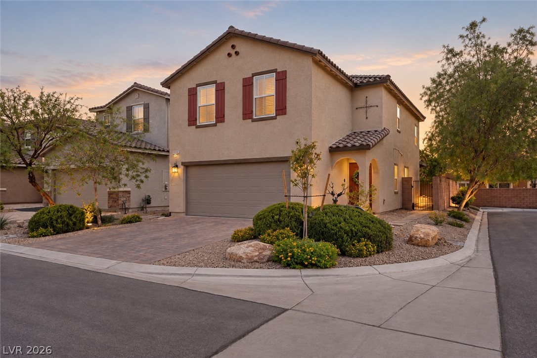 Two-story stucco home with red shutters, a wide garage, and desert landscaping at golden hour.