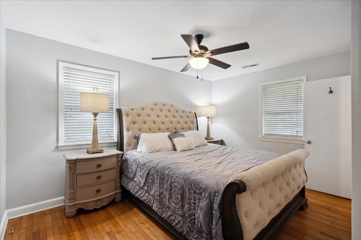 Furnished bedroom with a tufted bed, ceiling fan, and hardwood floors.