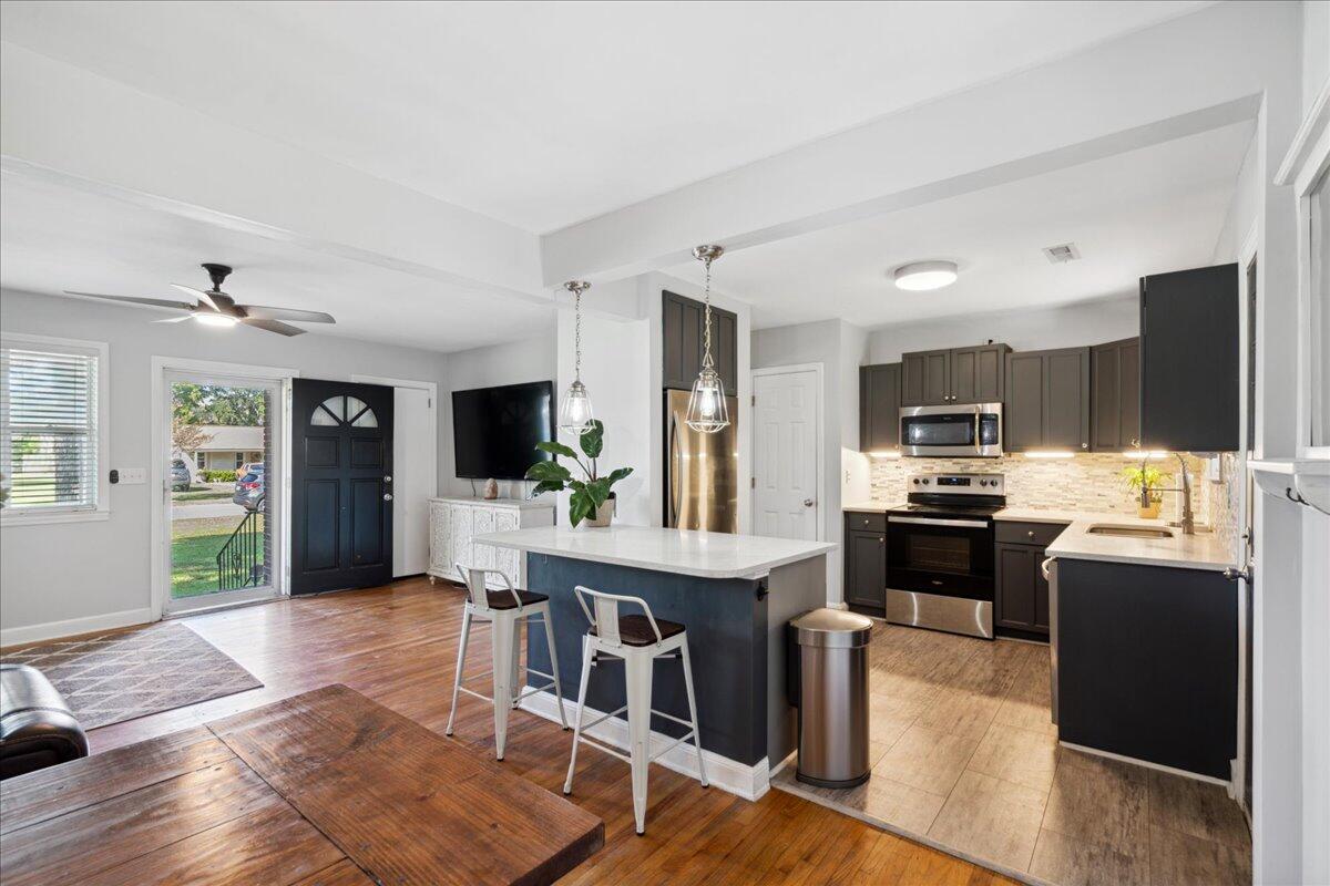 Open kitchen with a large island, dark cabinets, stainless steel appliances, and wood floors.