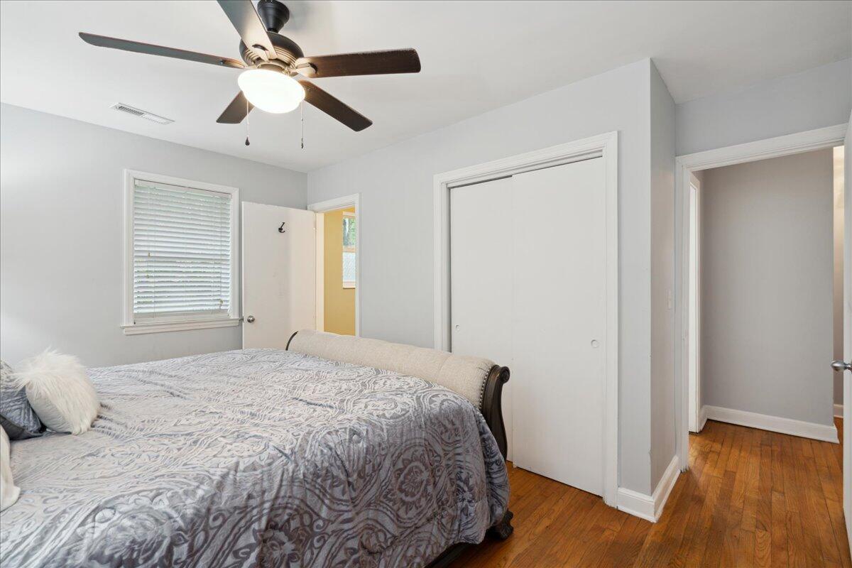 Bedroom with a patterned bedspread, ceiling fan, window blinds, and hardwood floors.