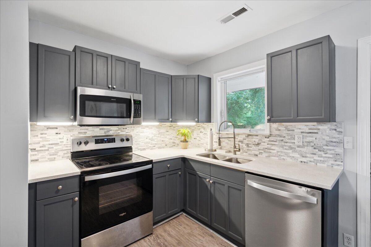 Kitchen with dark gray cabinets, stainless steel appliances, and a mosaic backsplash beneath a window.