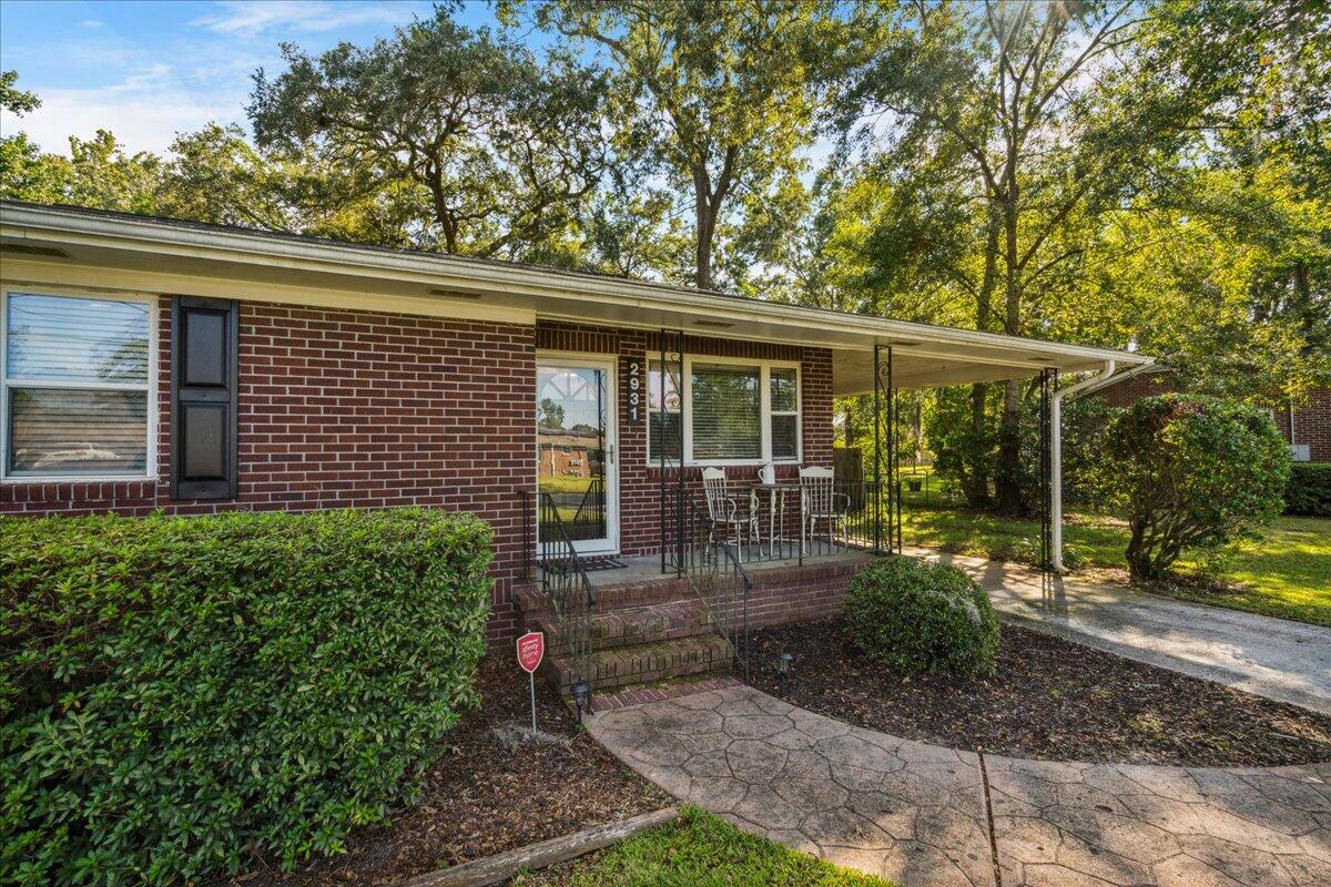 Single-story brick ranch with a covered porch, brick steps, and mature trees.