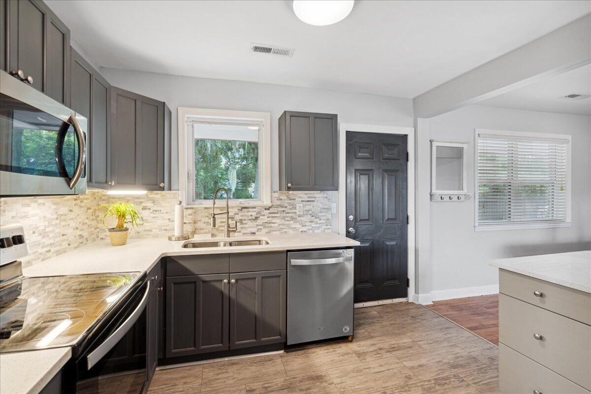Kitchen with dark gray cabinets, white counters, a tiled backsplash, and stainless steel appliances.