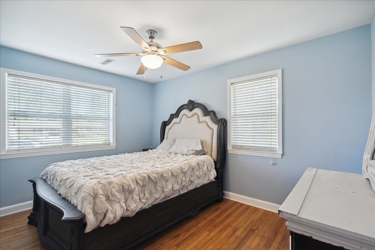 Bedroom with a dark wooden bed, light blue walls, white blinds, and hardwood floors.