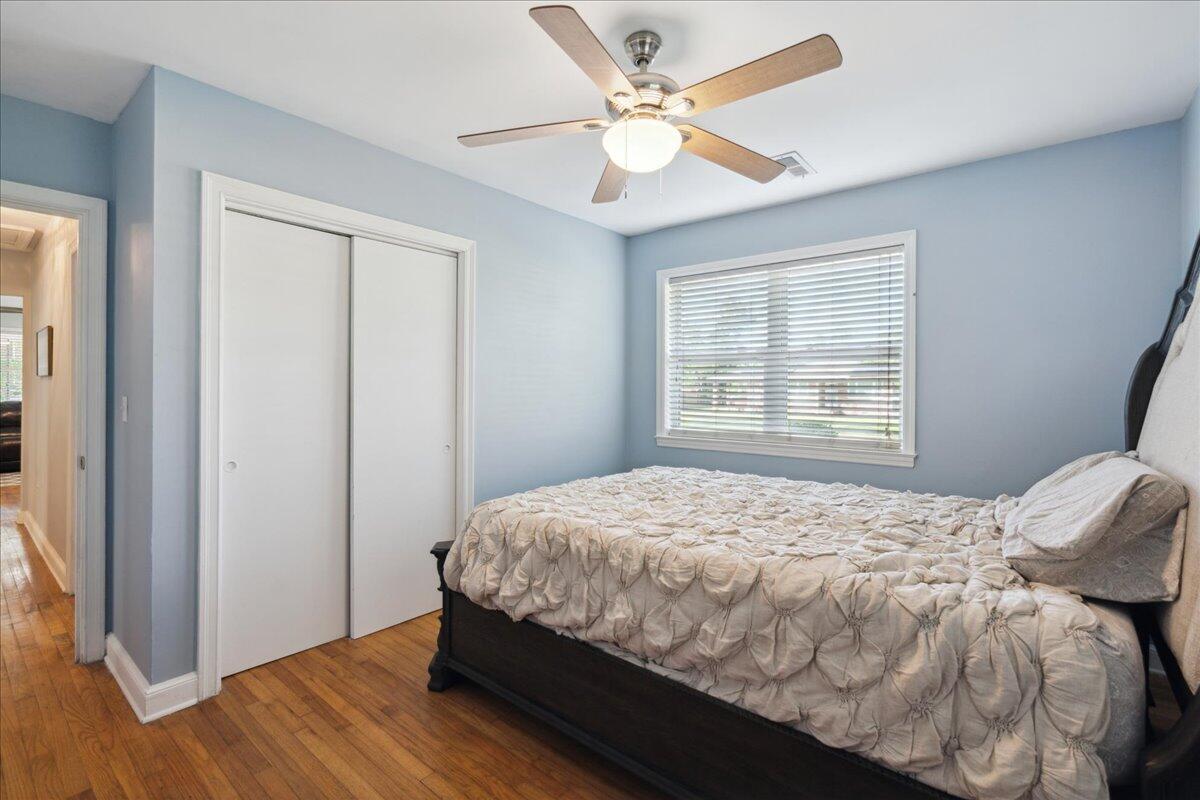 Bedroom with pale blue walls, hardwood floors, a bed, sliding-door closet, and ceiling fan.