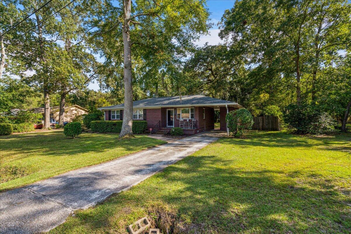 Brick ranch home with a covered carport, long driveway, broad lawn, and mature trees.