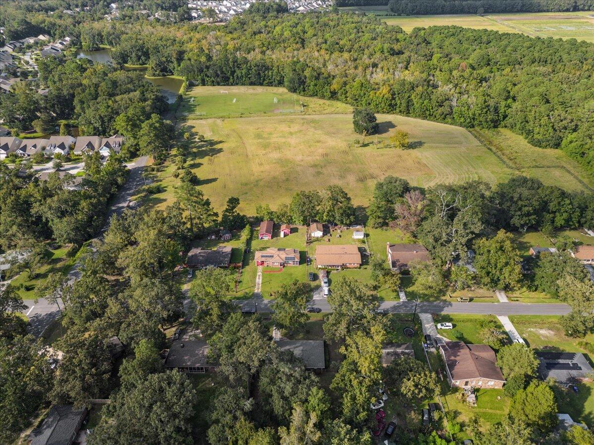 Aerial view of a large open field bordered by woods, with homes and a road in the foreground.