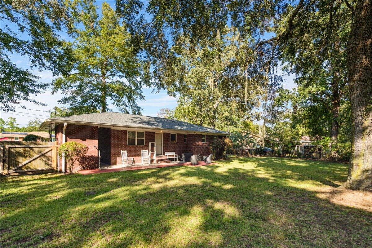 Red brick home's backyard, with patio chairs, a broad lawn, and mature shade trees.
