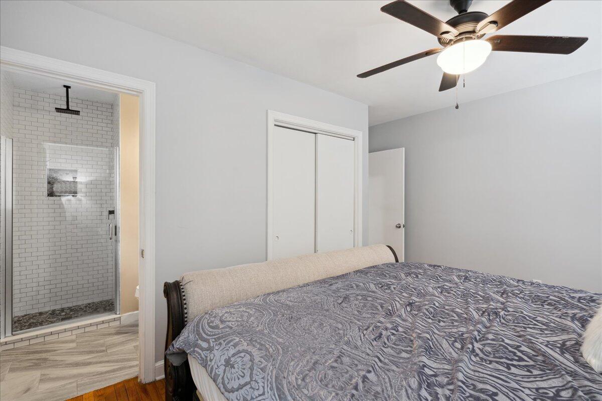 Bedroom with a patterned gray bedspread and an adjoining white subway-tile shower.