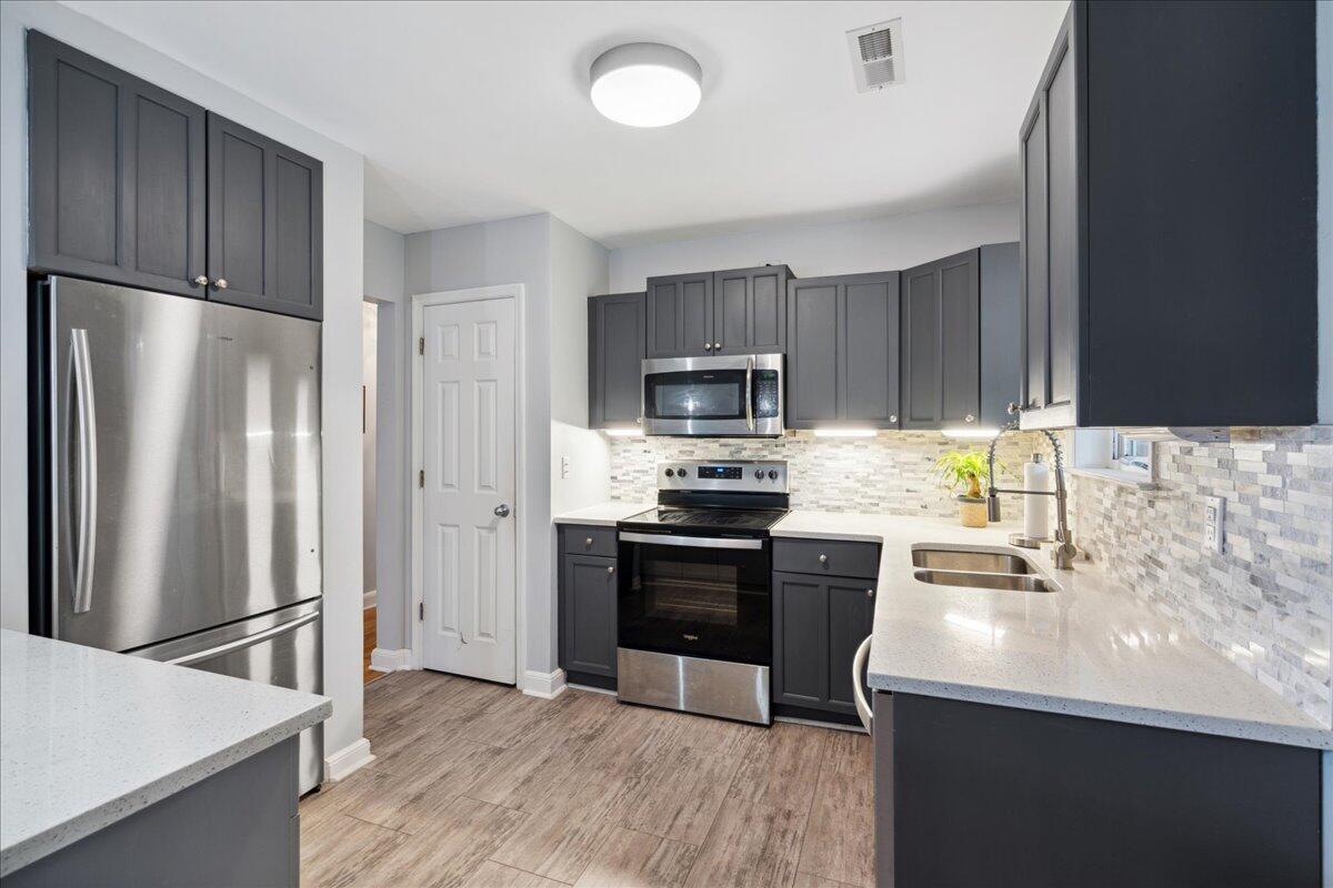 Kitchen with dark gray cabinets, stainless steel appliances, white countertops, and a mosaic tile backsplash.