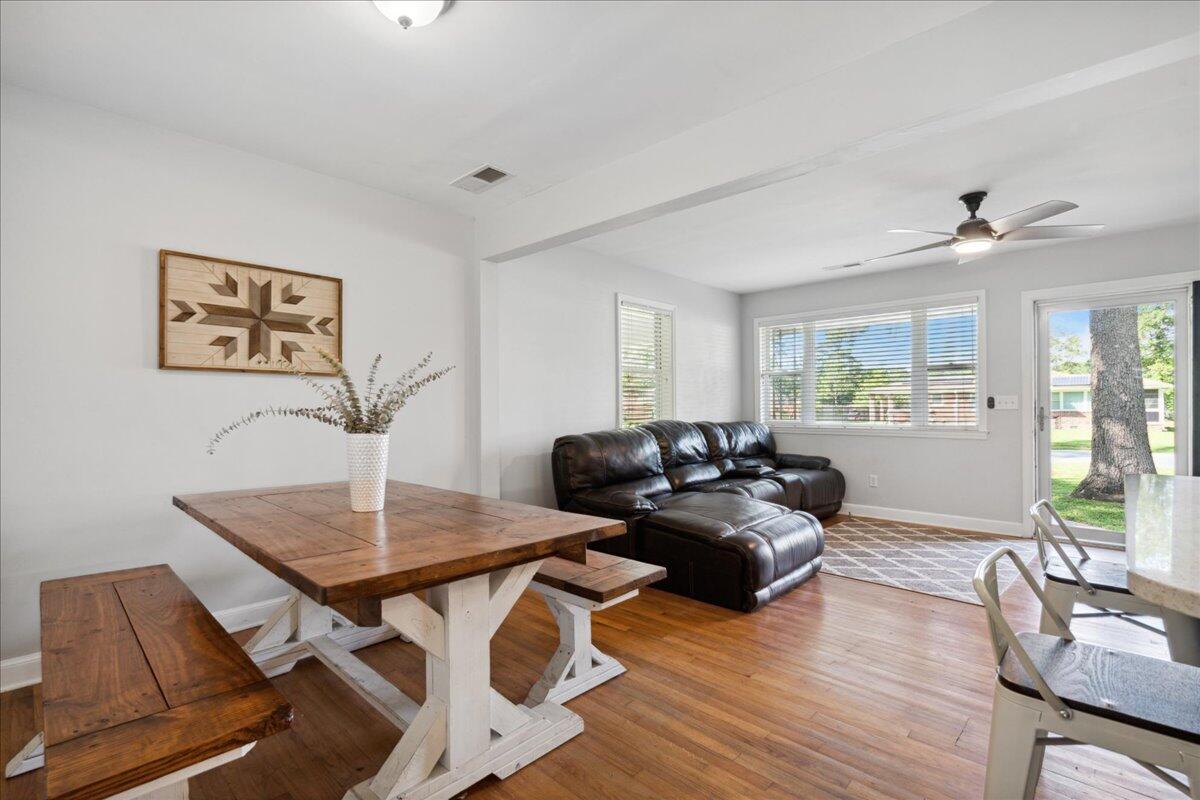 Dining and living area with a farmhouse table, leather sectional, hardwood floors, and large windows.
