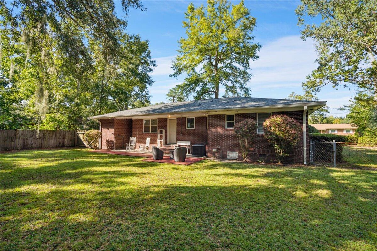 Brick home's rear patio with chairs overlooks a spacious, tree-shaded lawn.