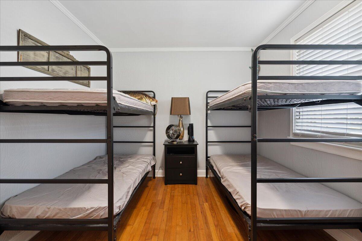 Bedroom with two metal bunk beds, a central nightstand, hardwood floors, and a window with blinds.